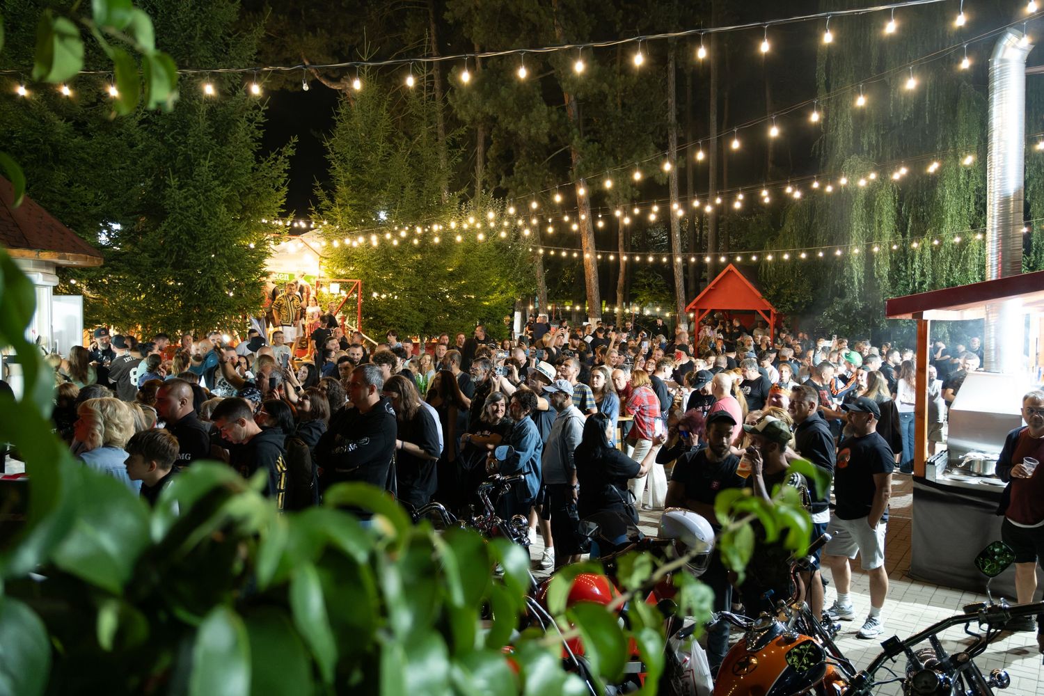Large crowd gathered at an outdoor nighttime motorcycle rally event with string lights overhead.