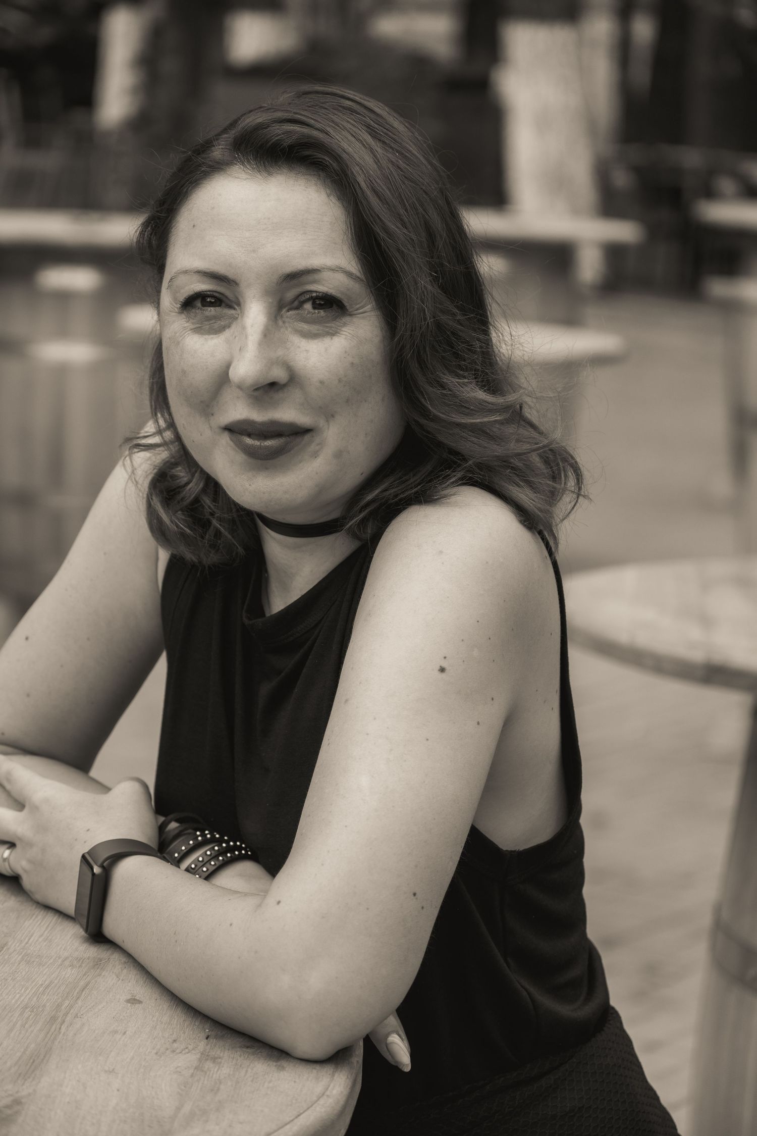 Black and white portrait of a woman in sleeveless black top leaning on wooden surface.