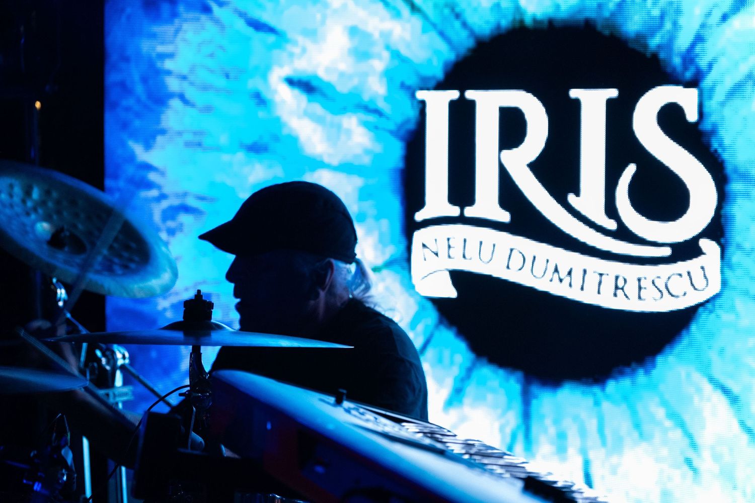 Silhouette of drummer against blue Iris Nelu Dumitrescu band logo projection screen.