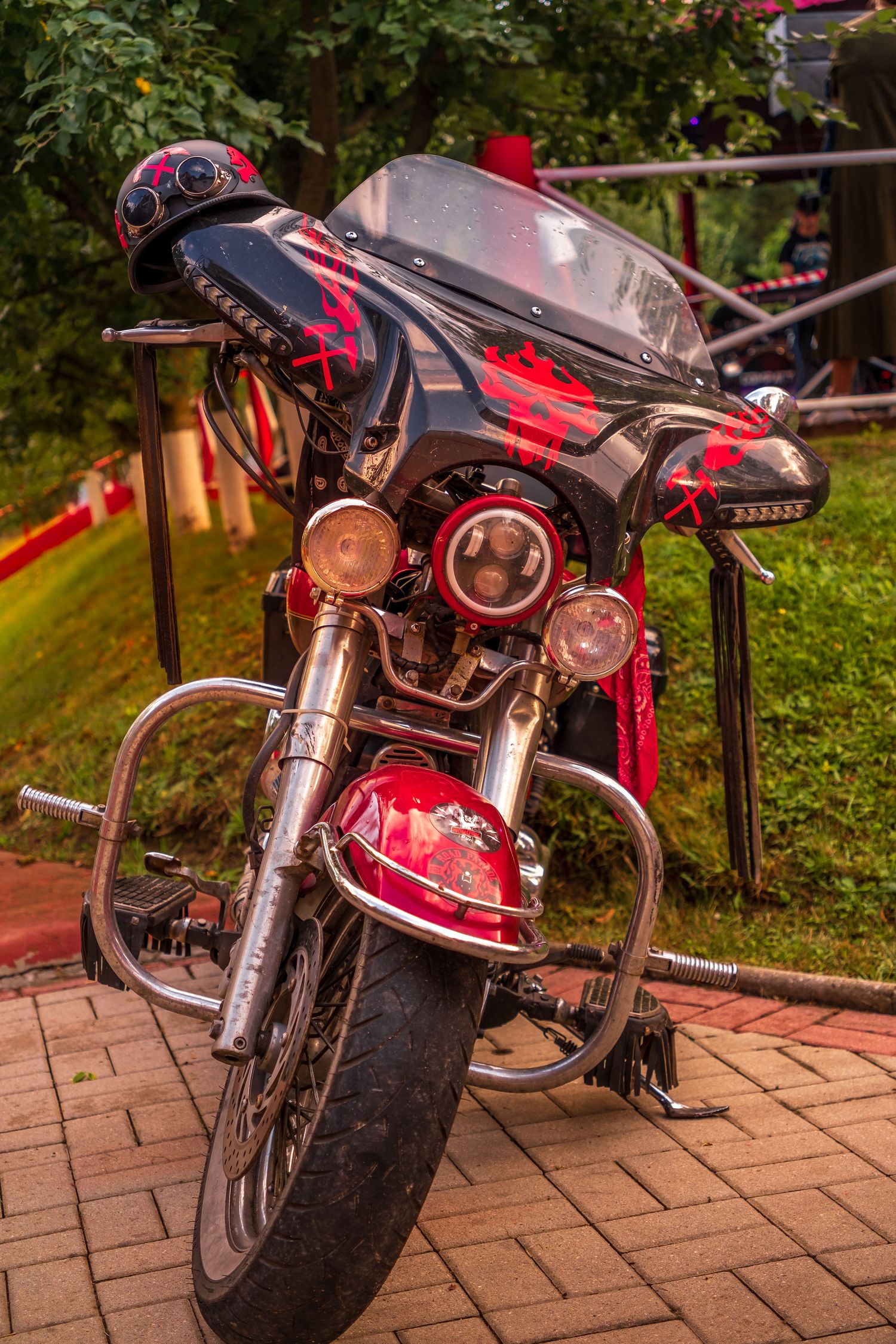 Custom red and black Harley-Davidson motorcycle with decorative paint job parked on brick pavement outdoors.