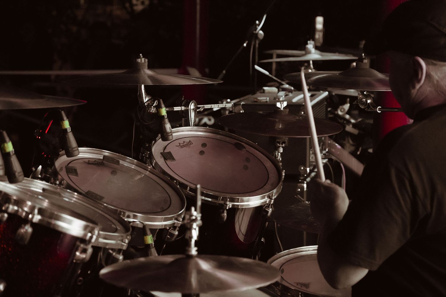 Close-up of drummer playing red drum kit during a live rock concert performance.