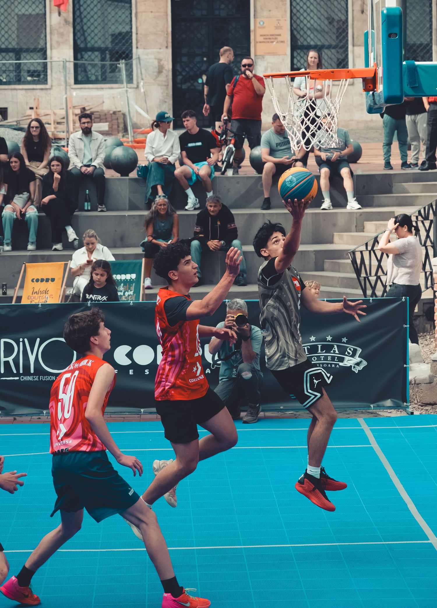 Players competing in an intense outdoor street basketball game on a blue court.