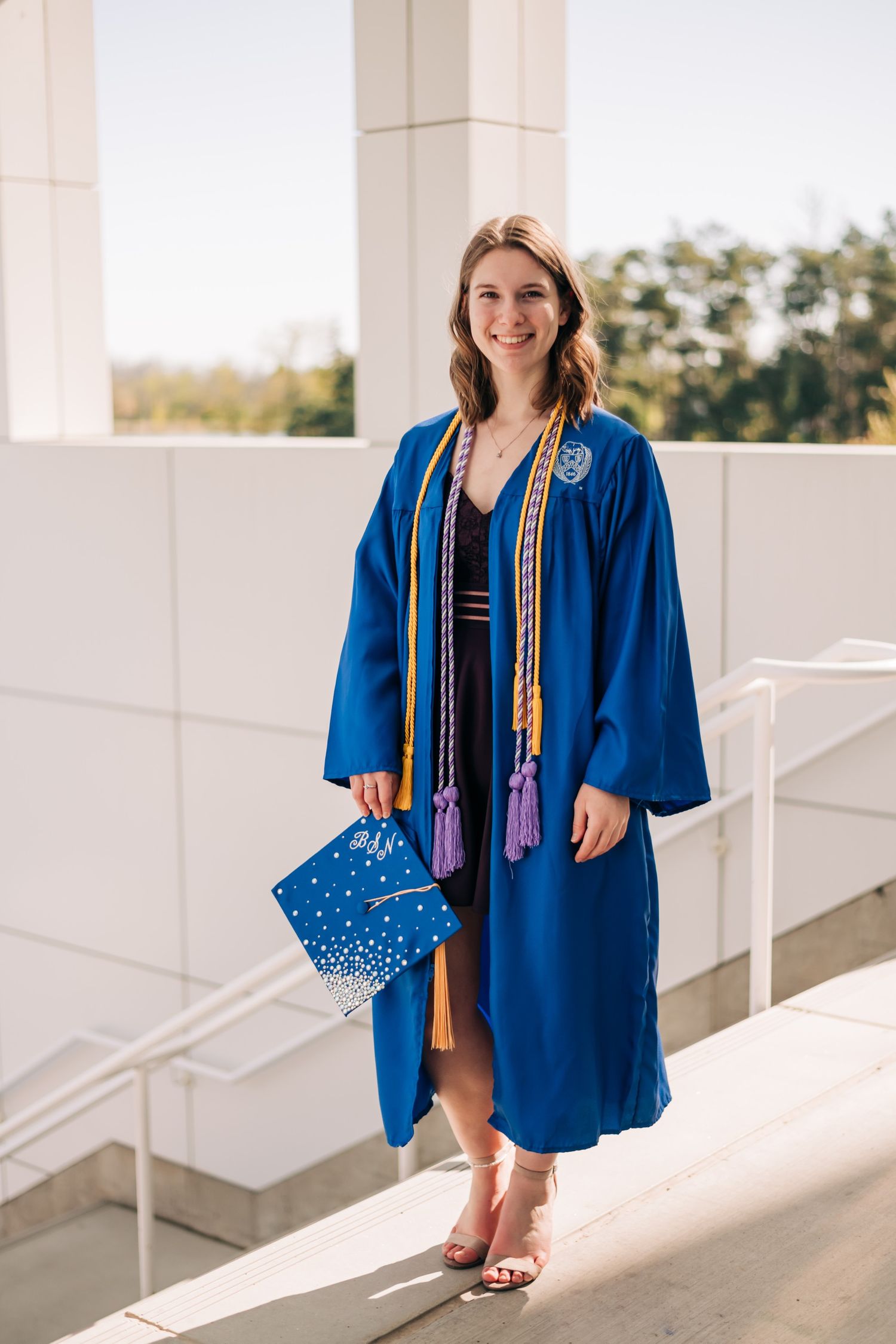 female college graduate wearing blue graduation gown with yellow cords