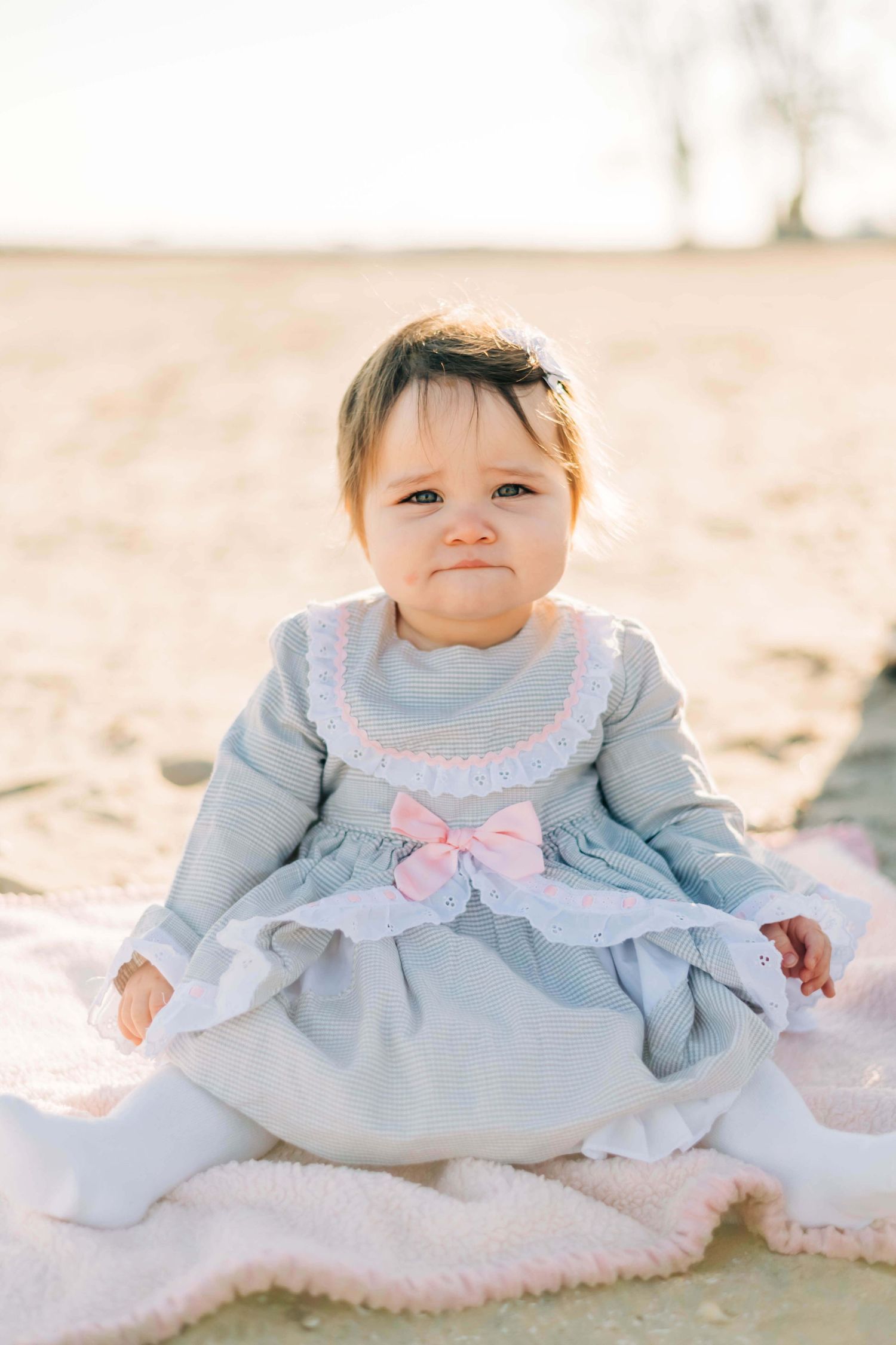 Photo of baby girl in a blue dress sitting in the sand at a beach