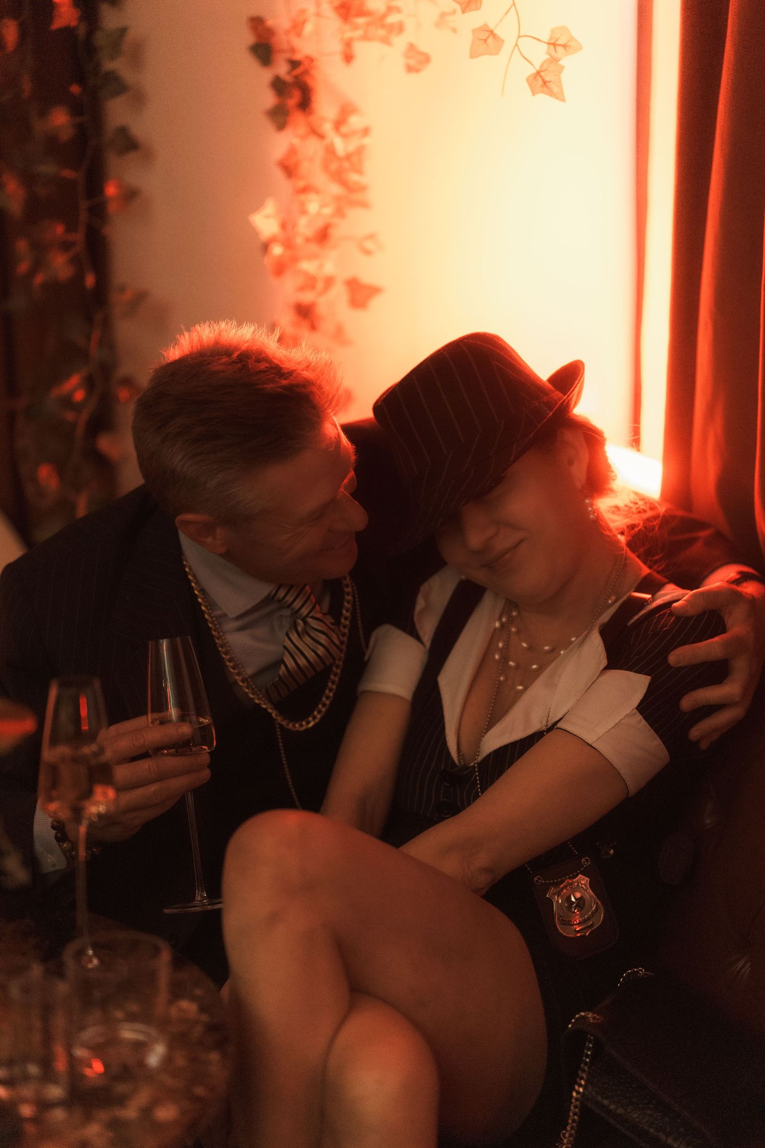 Couple sitting together in warm red-lit room with champagne glasses.