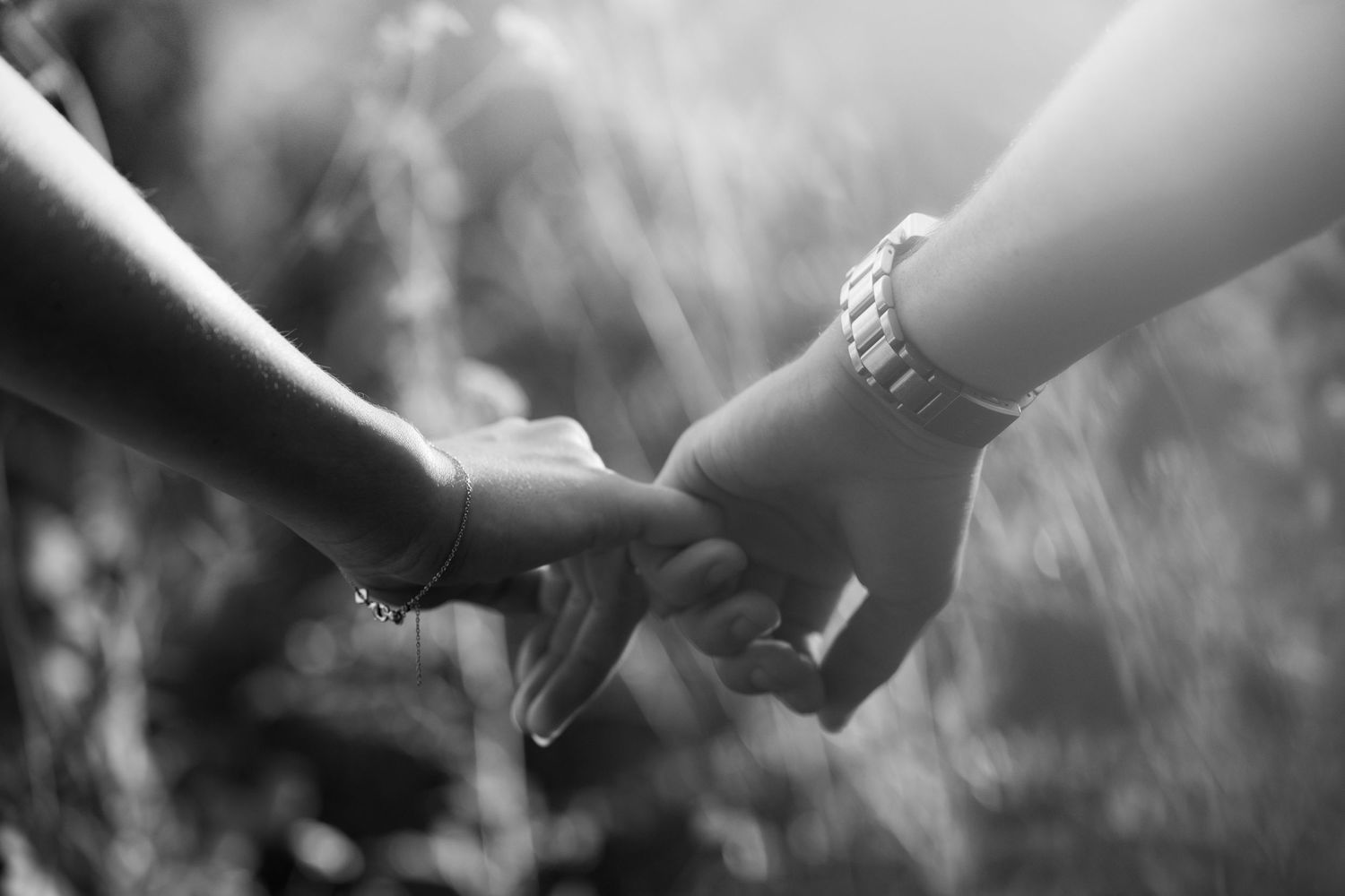 Black and white close-up of couple holding hands outdoors with bokeh background.