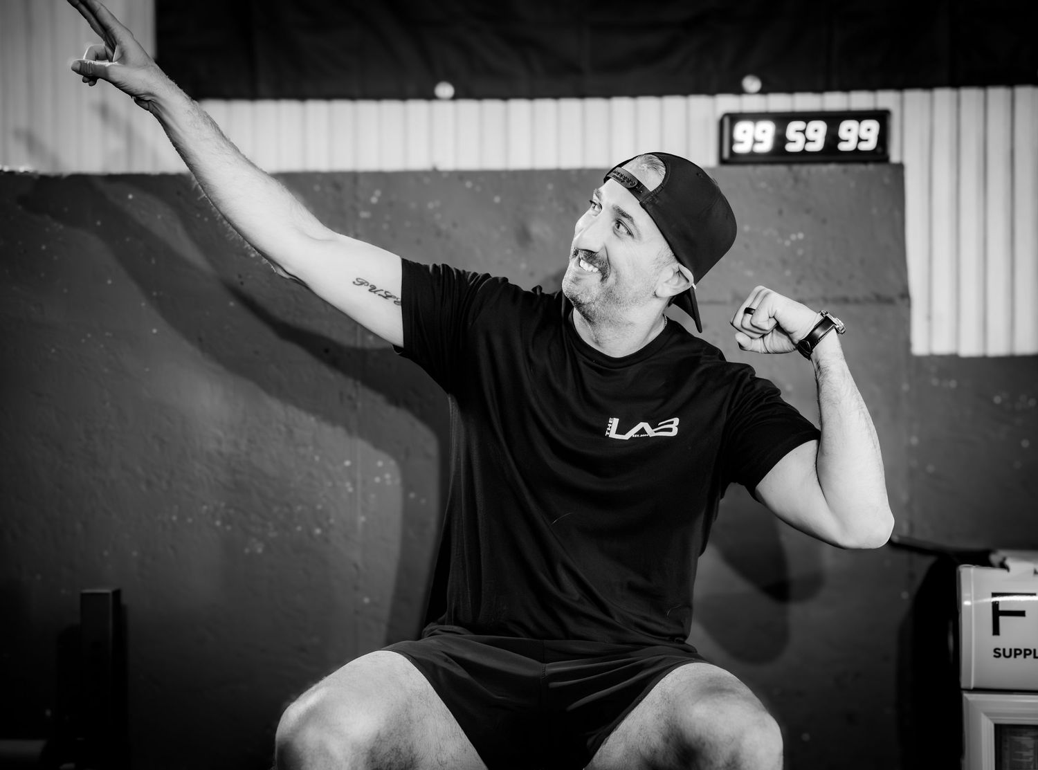 Branding - The Lab - athletic man in black workout gear stretching arm upward in gym, black and white.