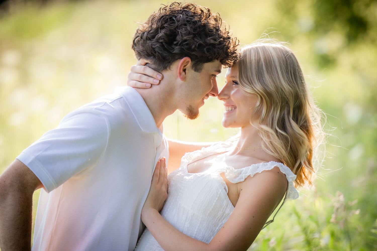 Happy couple touching foreheads and smiling in a bright sunny meadow.