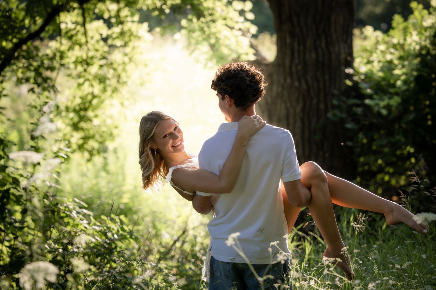 Man lifting woman in his arms in a sunny green forest clearing.