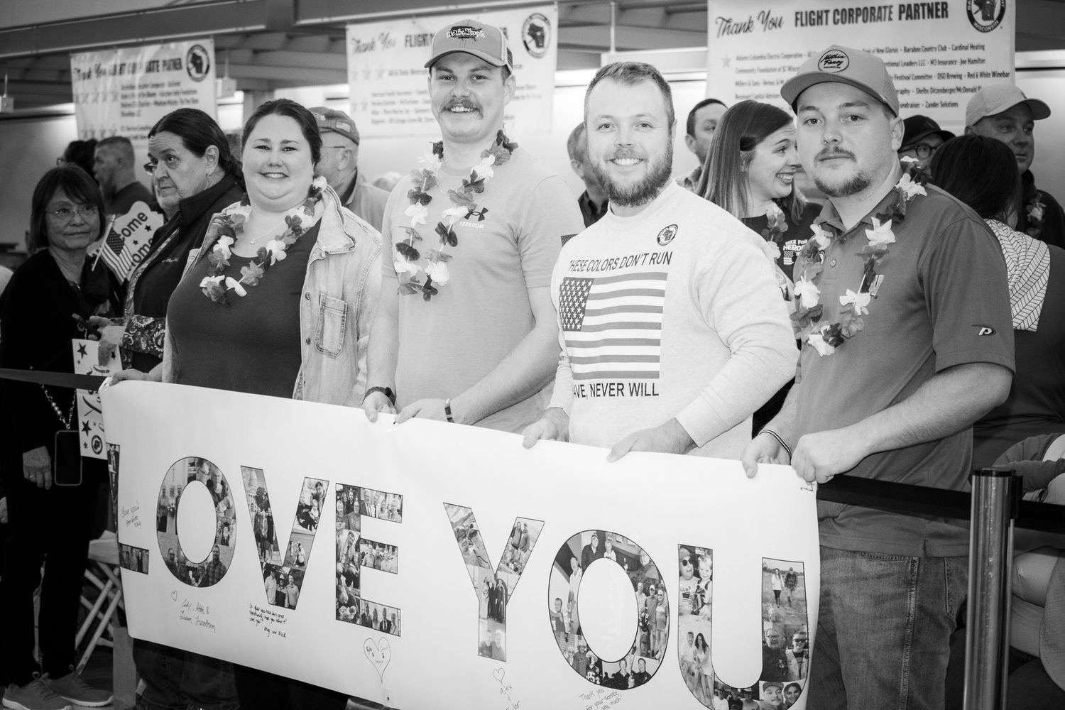 Group of people holding a Love You banner at an airport welcome home event in black and white.