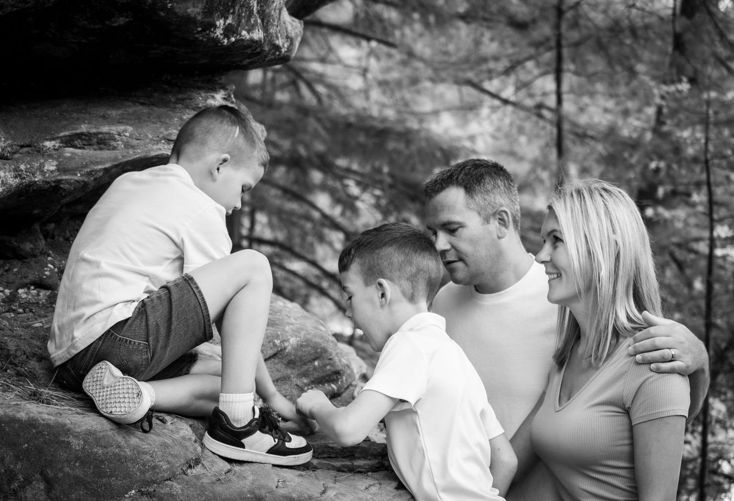 Black and white photo of a loving family with two boys sharing a tender moment on rocky terrain.