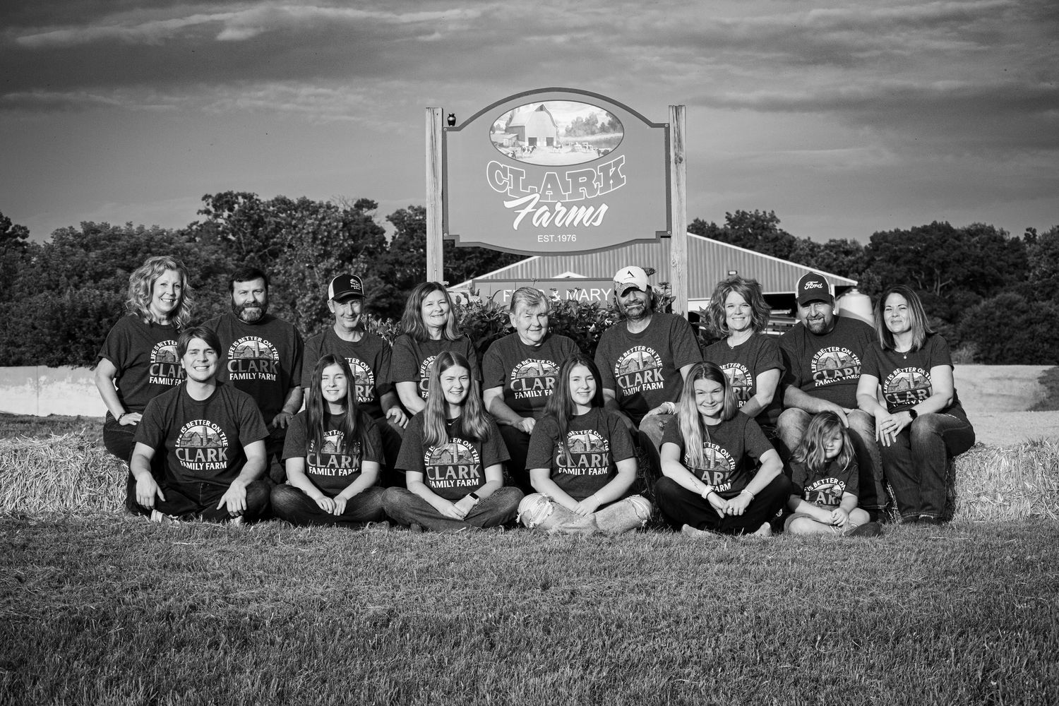 A large group of Clark Farms family members poses together on the grass in black and white.