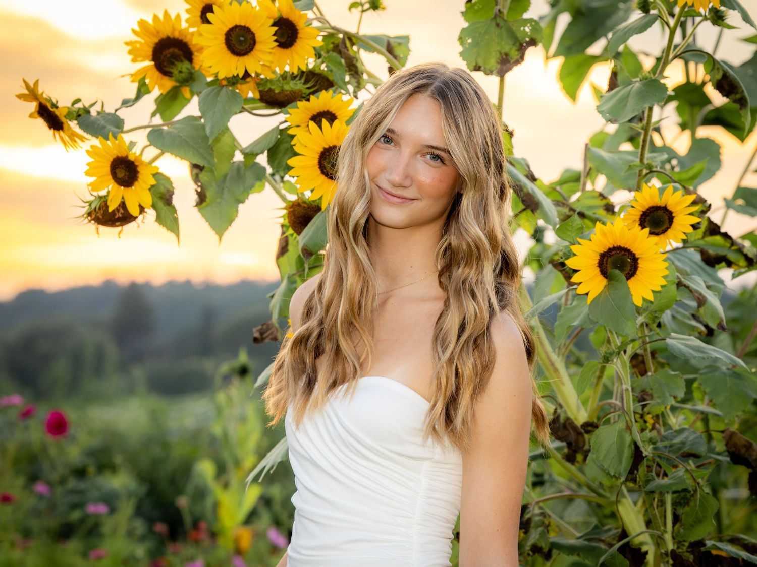 Young woman in white dress smiling among sunflowers at golden hour sunset in a lush garden.