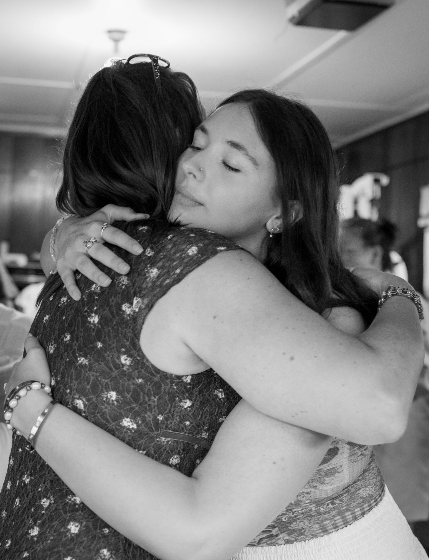 Two women sharing an emotional heartfelt hug at an indoor gathering, black and white.