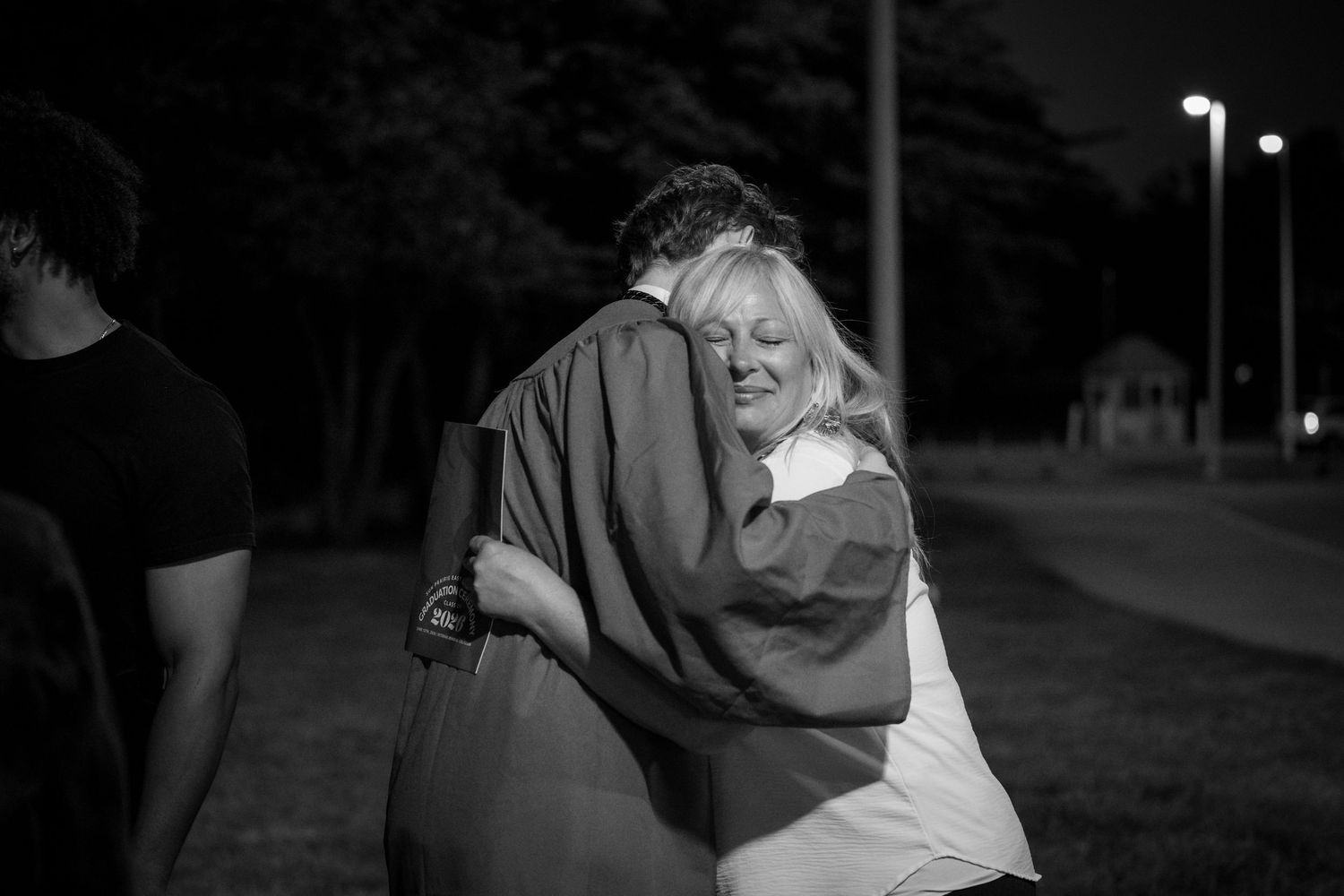 Black and white photo of two people sharing a warm embrace outdoors at night under street lights.