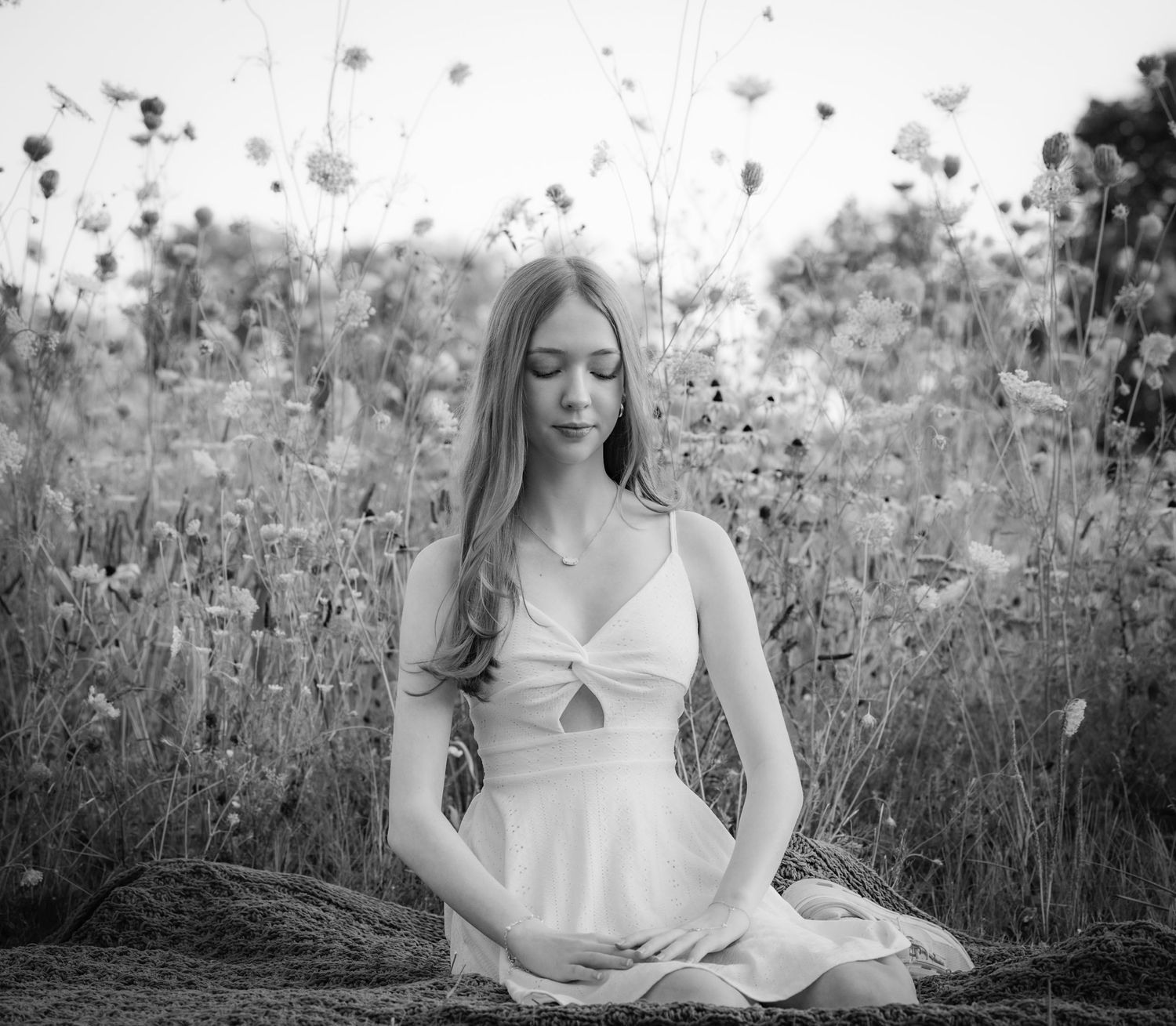 Young woman in white dress meditating peacefully in a wildflower field, black and white photography.