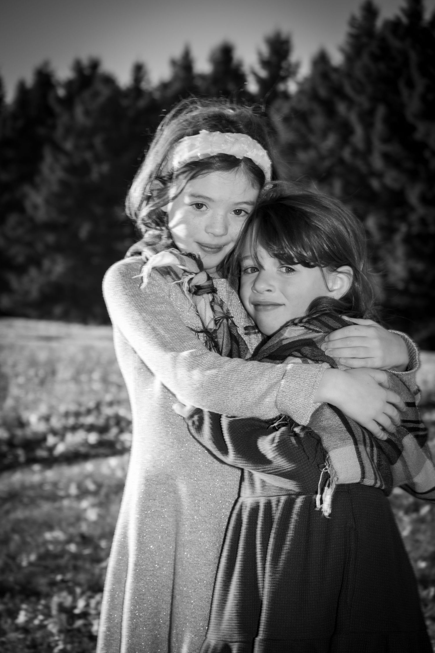 Two young girls hugging each other affectionately in black and white outdoor portrait among trees.