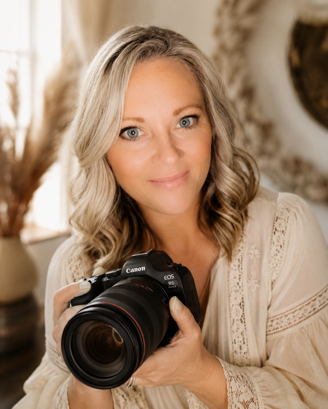 Professional female photographer holding Canon EOS camera with warm smile in cozy studio setting.