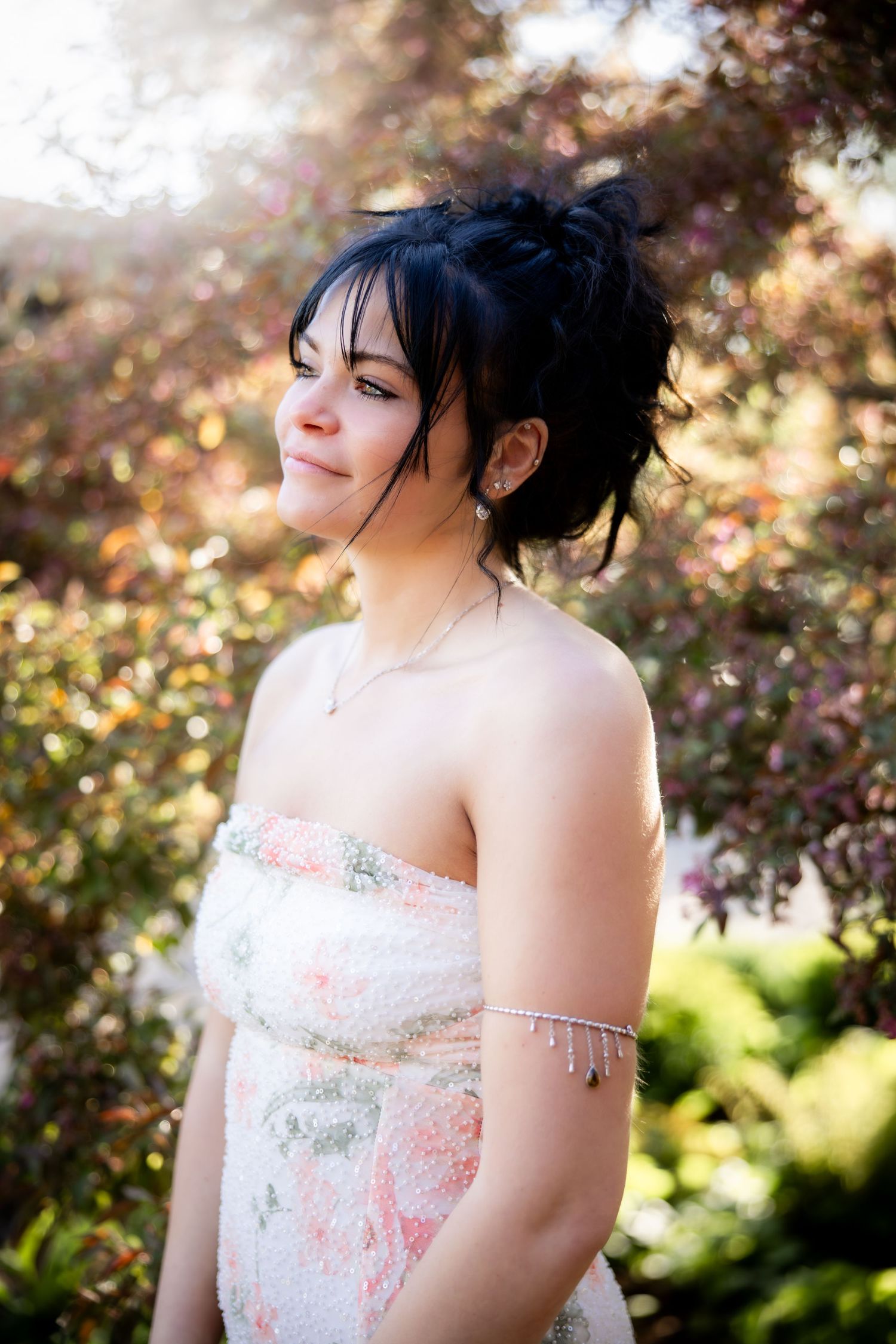 Young woman in strapless floral dress smiling outdoors among colorful autumn foliage.