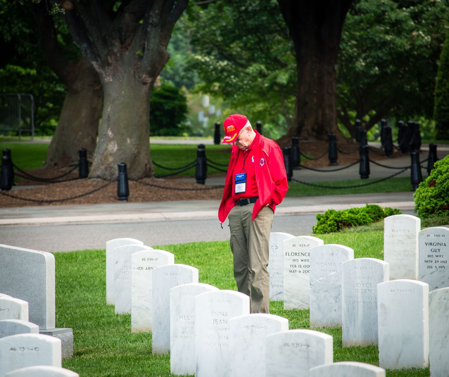 Man in red jacket standing solemnly among white headstones at a military cemetery.