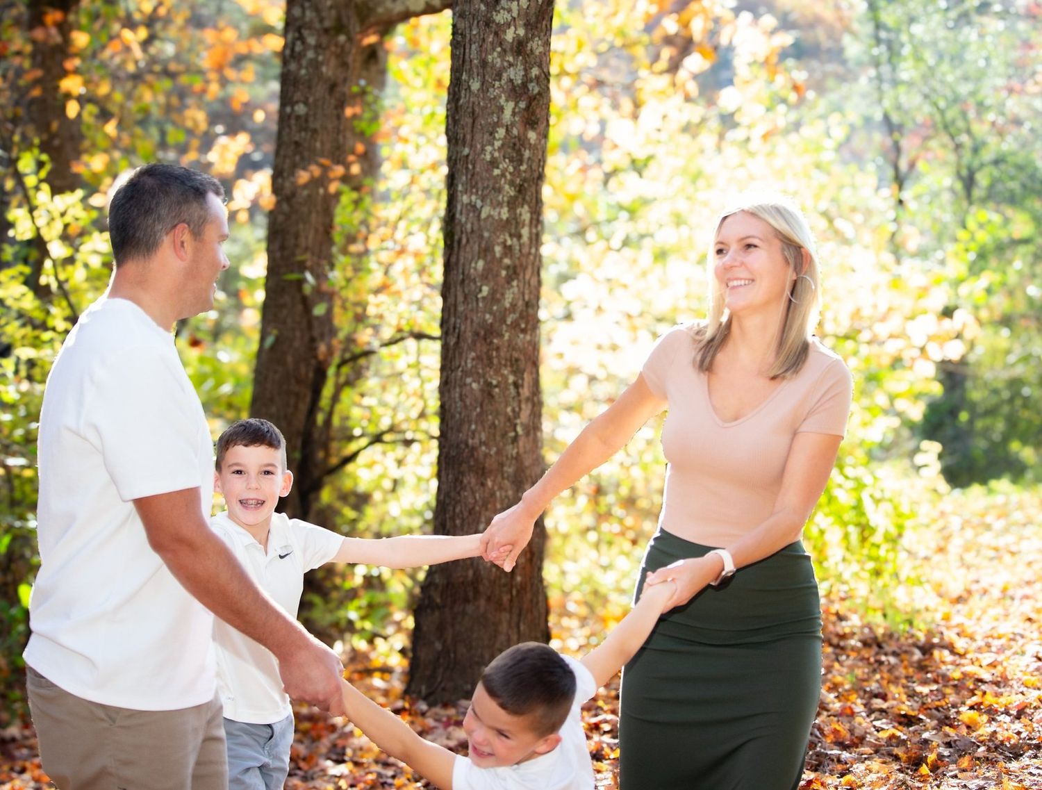Family of four holding hands and playing together in a sunny autumn forest.