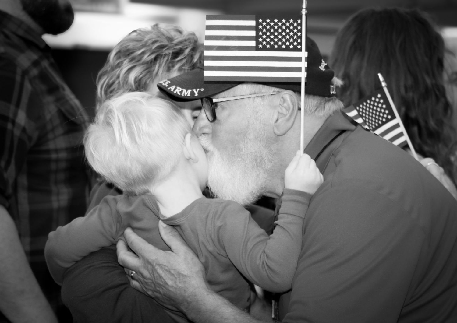 Elderly couple sharing a kiss at a military homecoming event with American flags in the background.