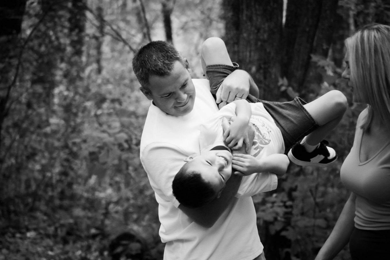 Father playfully lifts child upside down outdoors in black and white candid family photo.