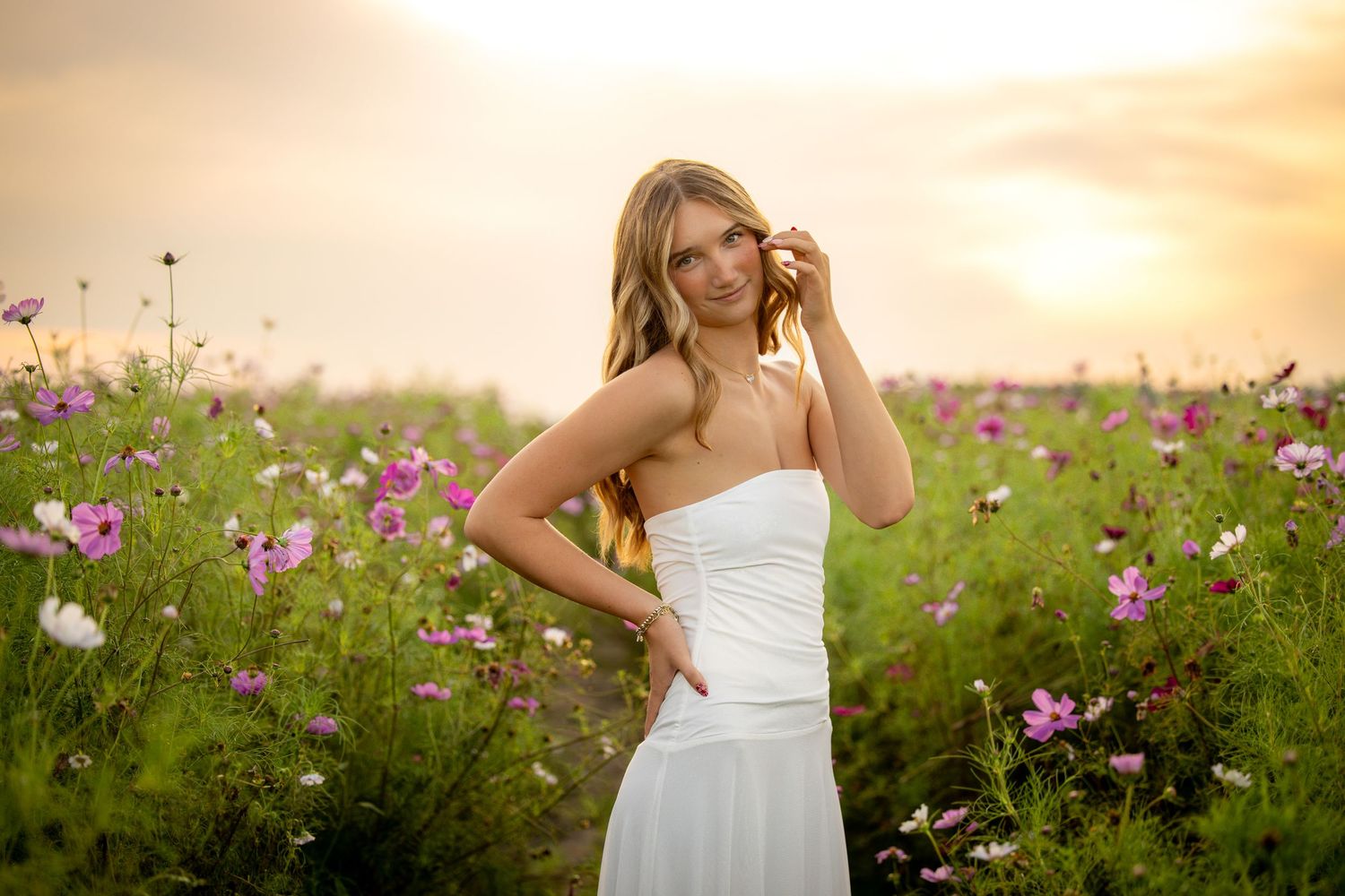 Young woman in white dress holding flower in vibrant pink cosmos field at golden sunset.