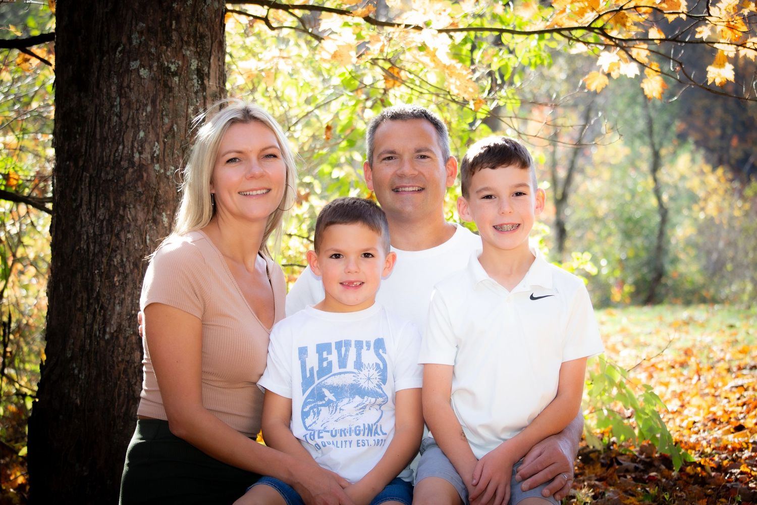 Smiling family of four sitting together under a tree during fall foliage season.