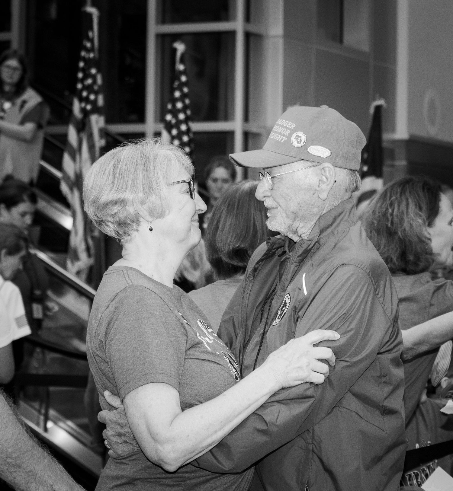 Badger Honor Flight - couple dancing and embracing at a patriotic event with American flags in background.