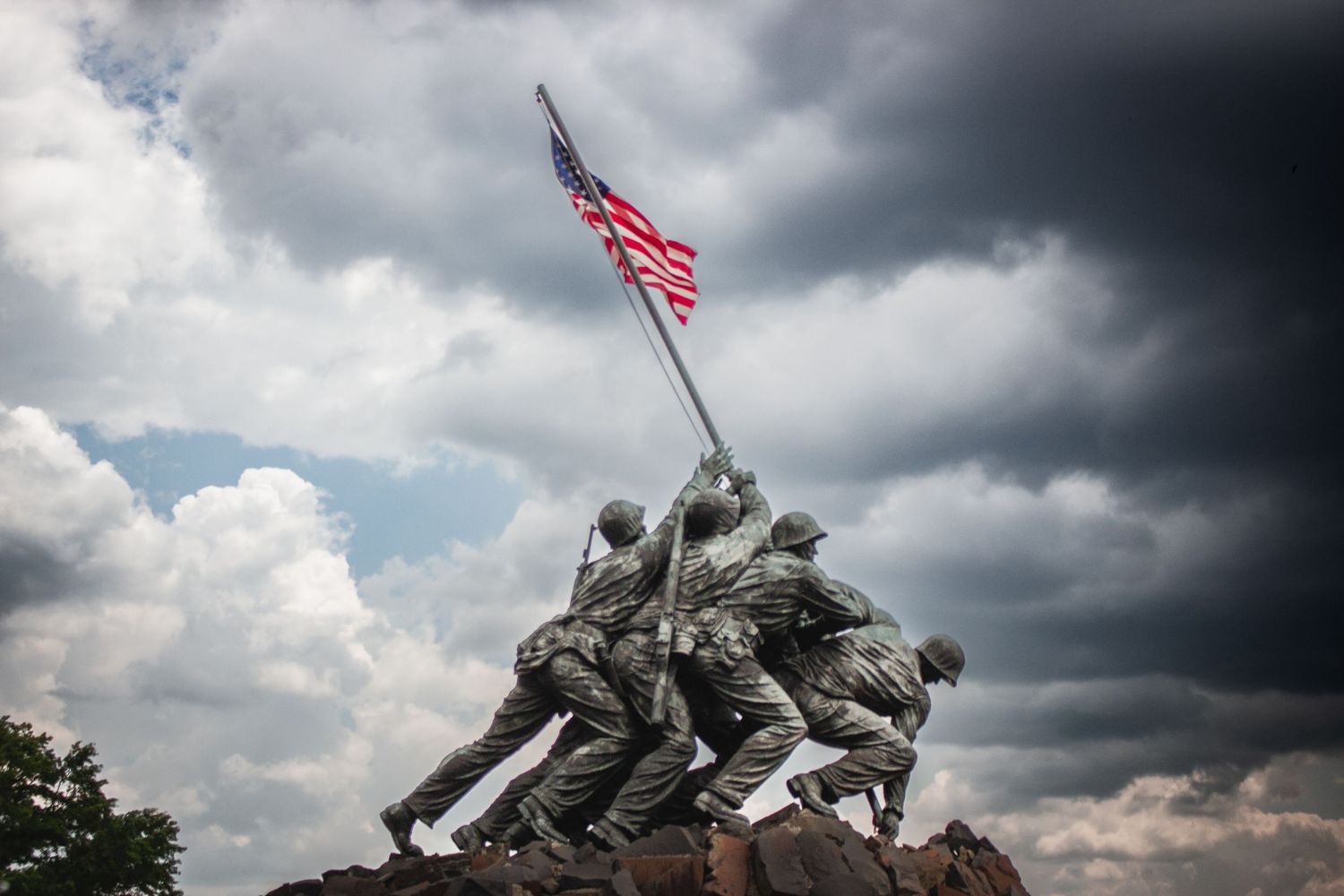 Iconic Iwo Jima Marine Corps War Memorial statue with American flag under dramatic cloudy sky.