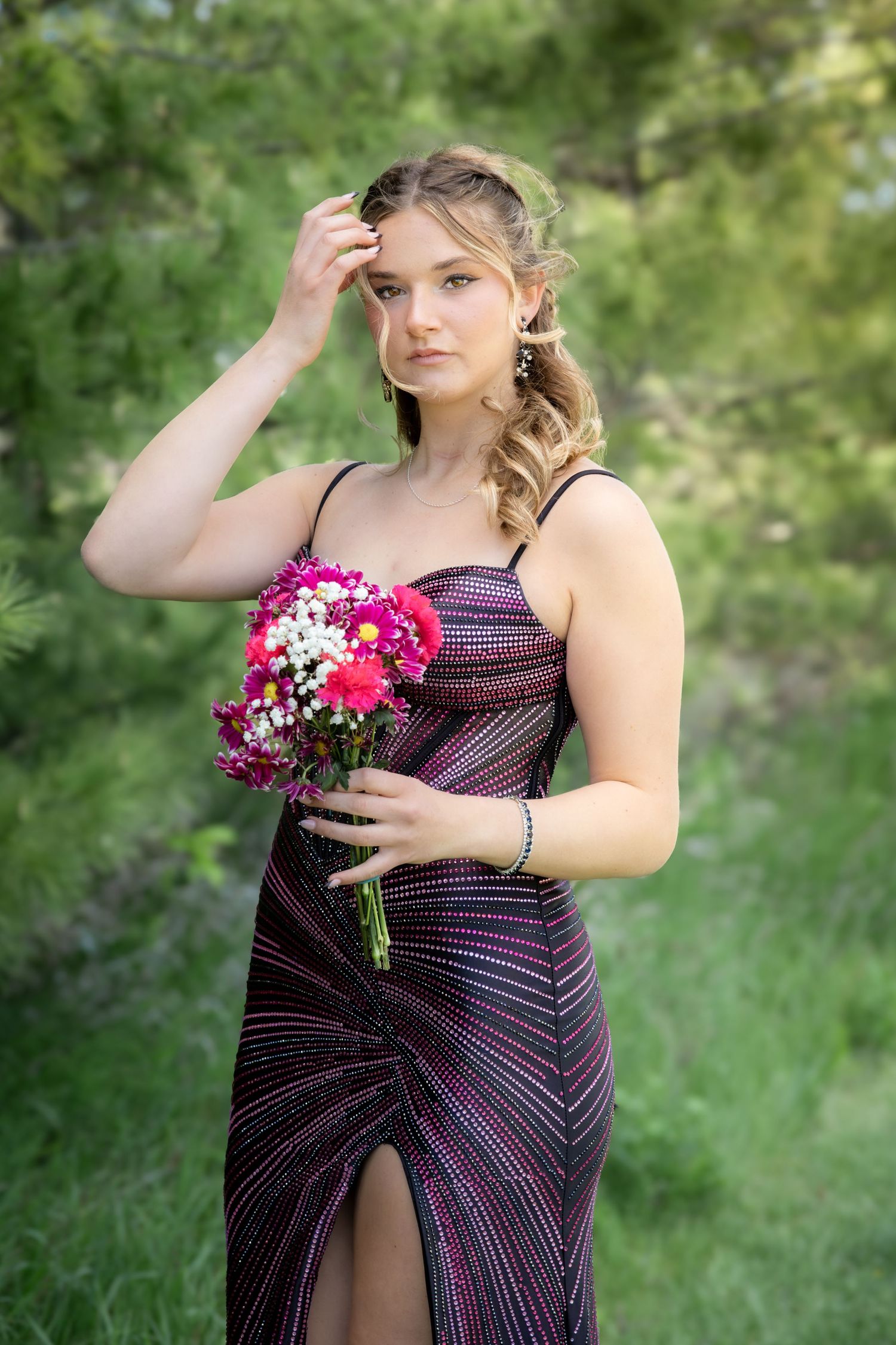 Young woman in sparkly dark prom dress holding pink flower bouquet outdoors.