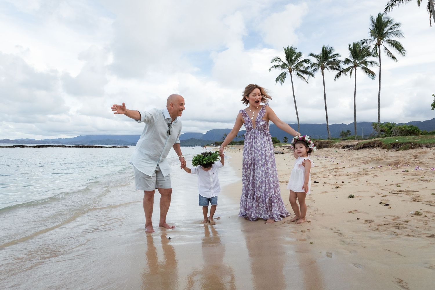 Family enjoying playful moment together while walking on tropical beach with palm trees.
