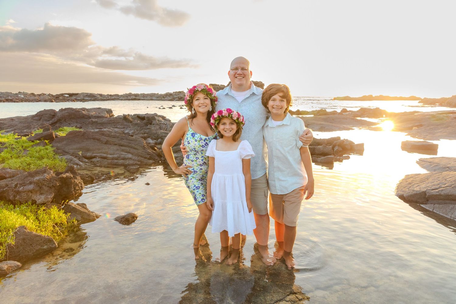 Family group poses together on wet volcanic rocks at sunset by the ocean.