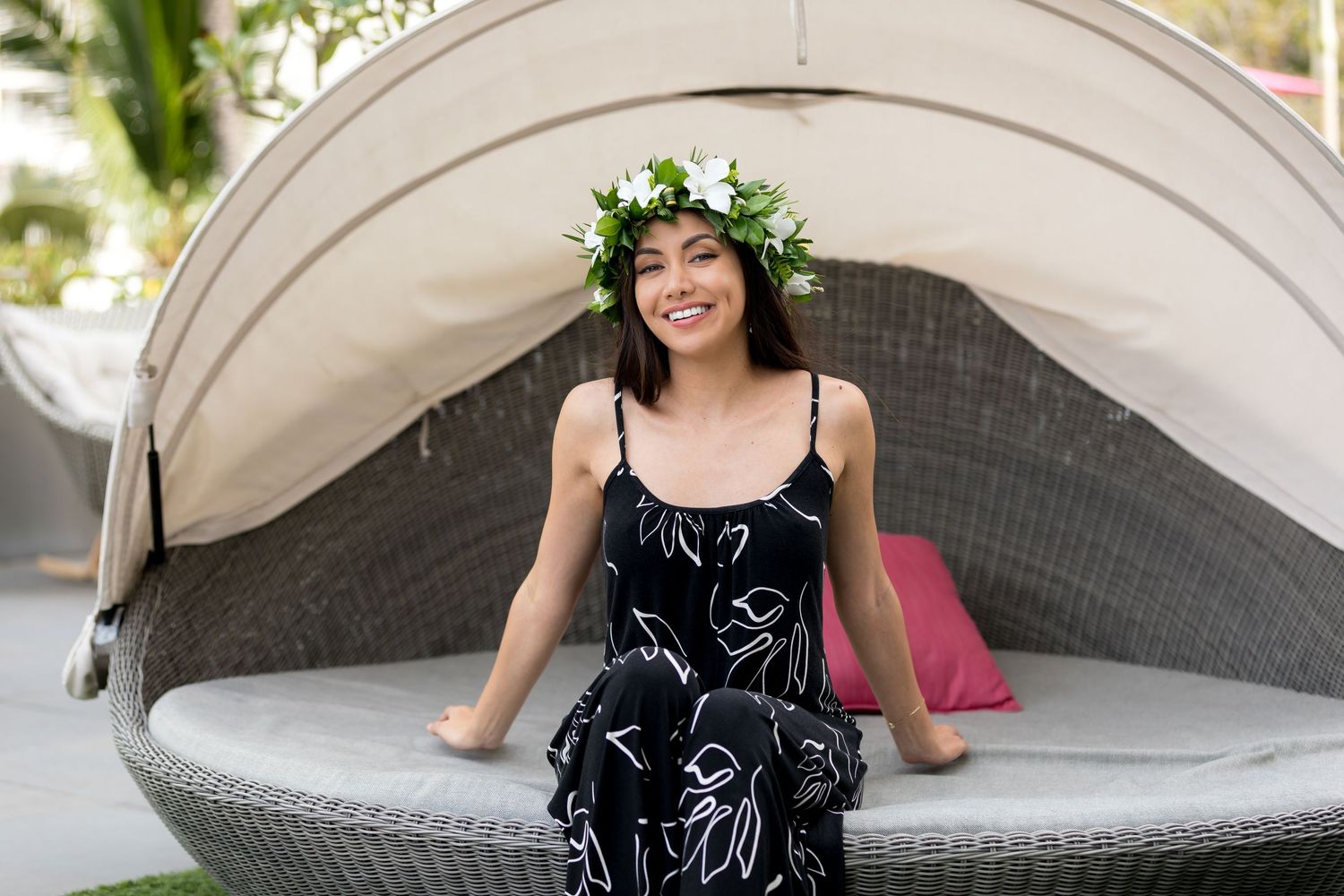 A person wearing a flower crown and black floral dress relaxes on a curved outdoor daybed.