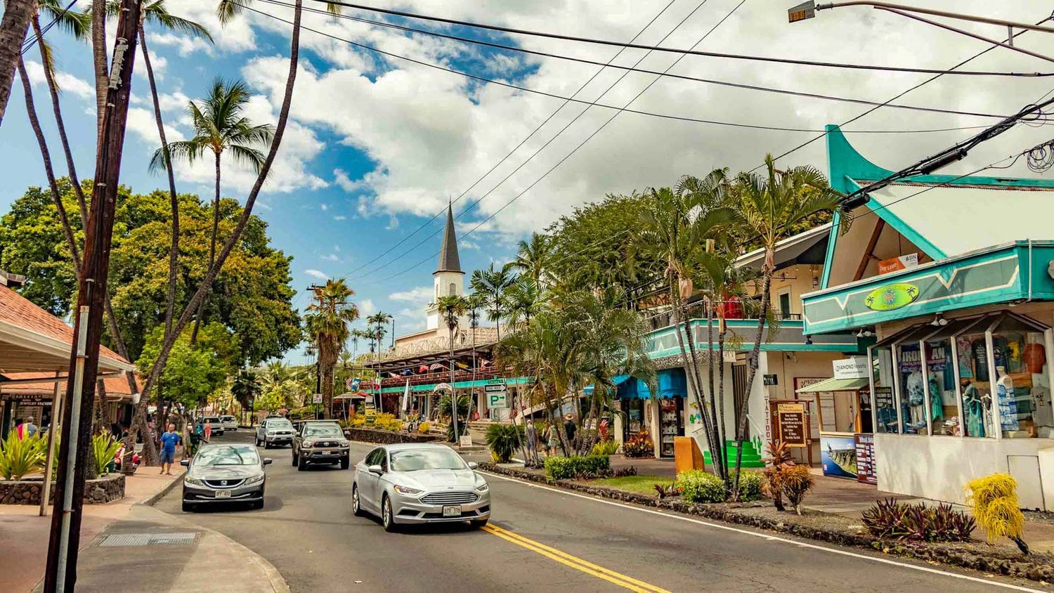 Colorful storefronts and palm trees line a sunny street in historic Paia town, Maui.