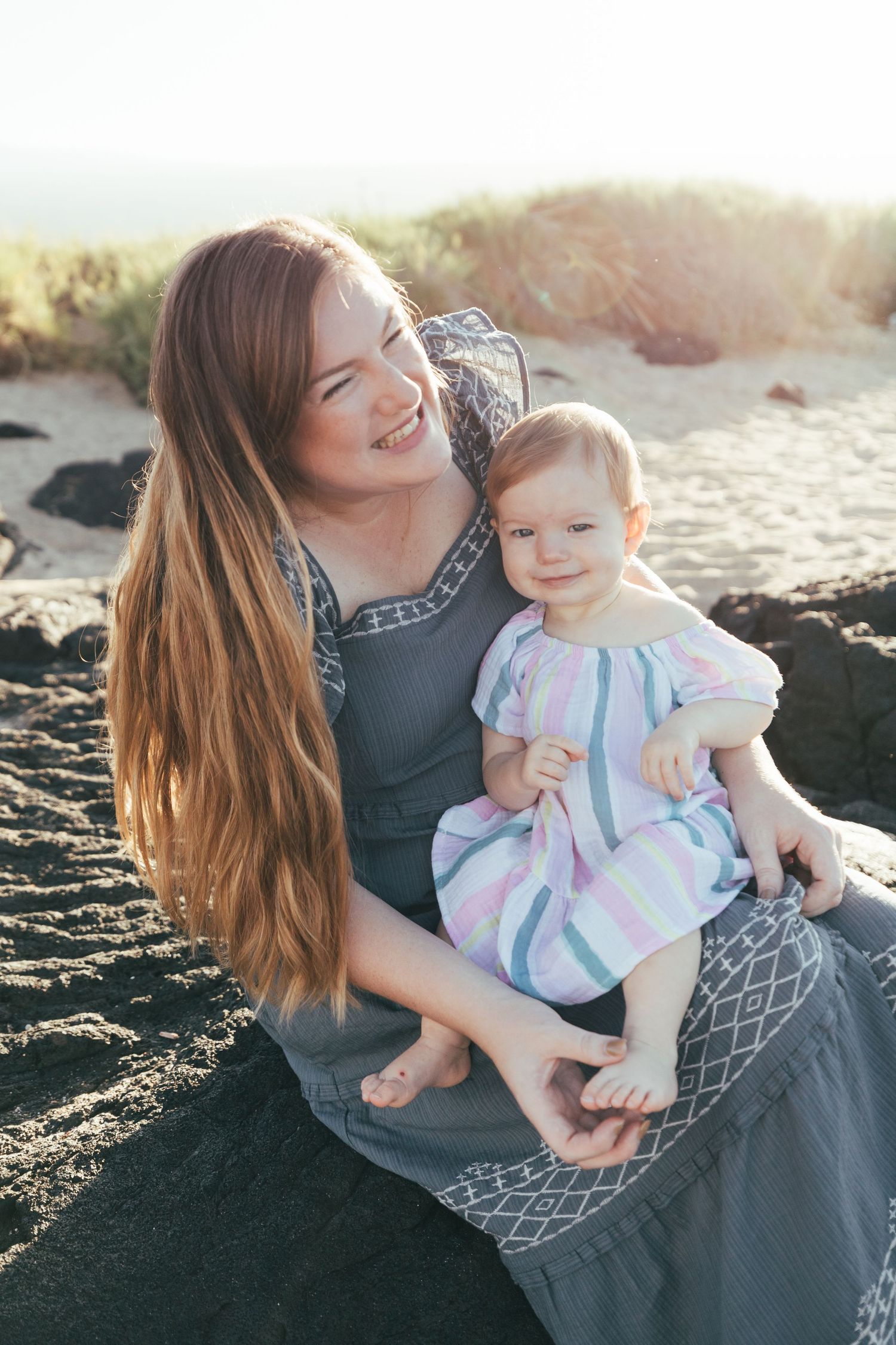 A tender moment between parent and child sitting on a rocky beach at sunset.