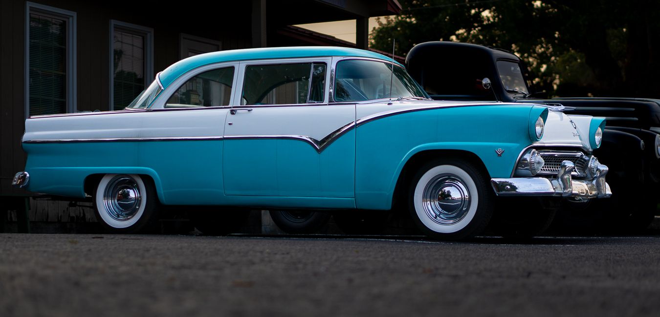 Vintage 1950s teal and white Ford classic car with chrome details and whitewall tires parked outdoors.