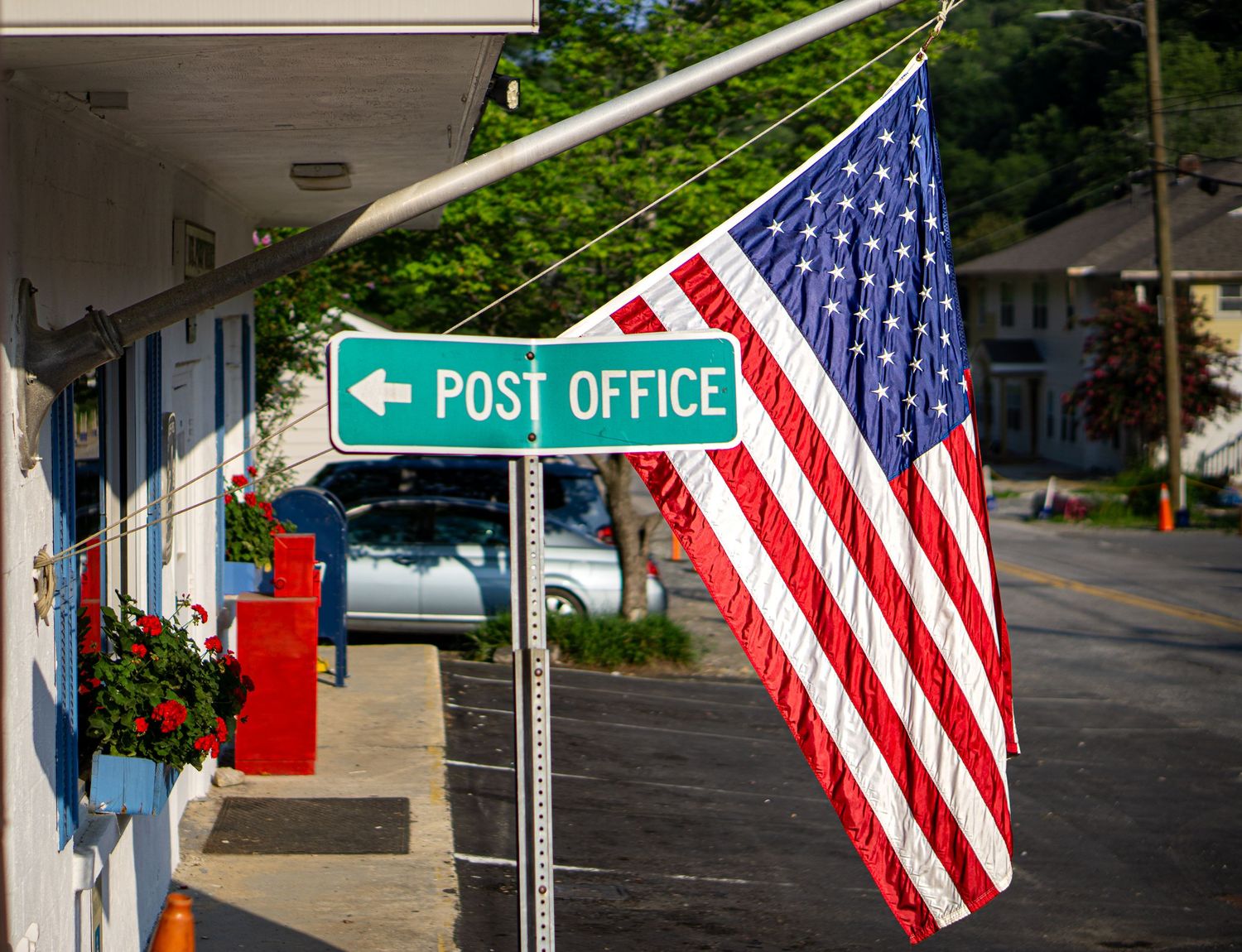 American flag hanging beside a green Post Office directional sign on a small town street.