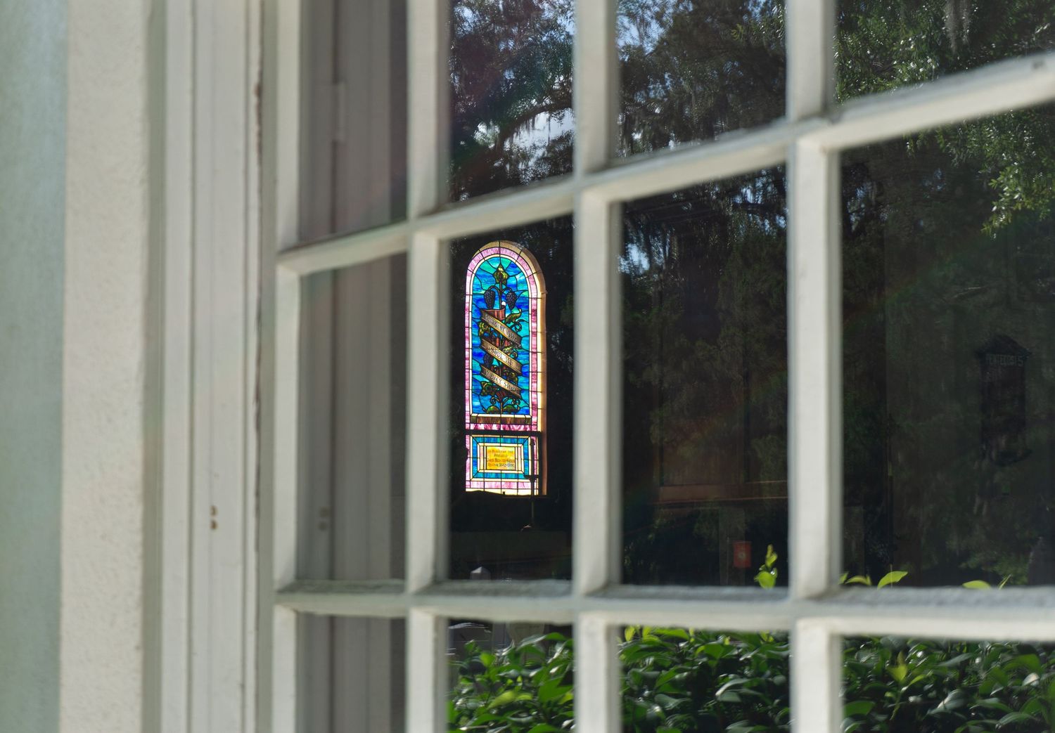 Colorful stained glass window panel visible through white-framed exterior window with garden view.