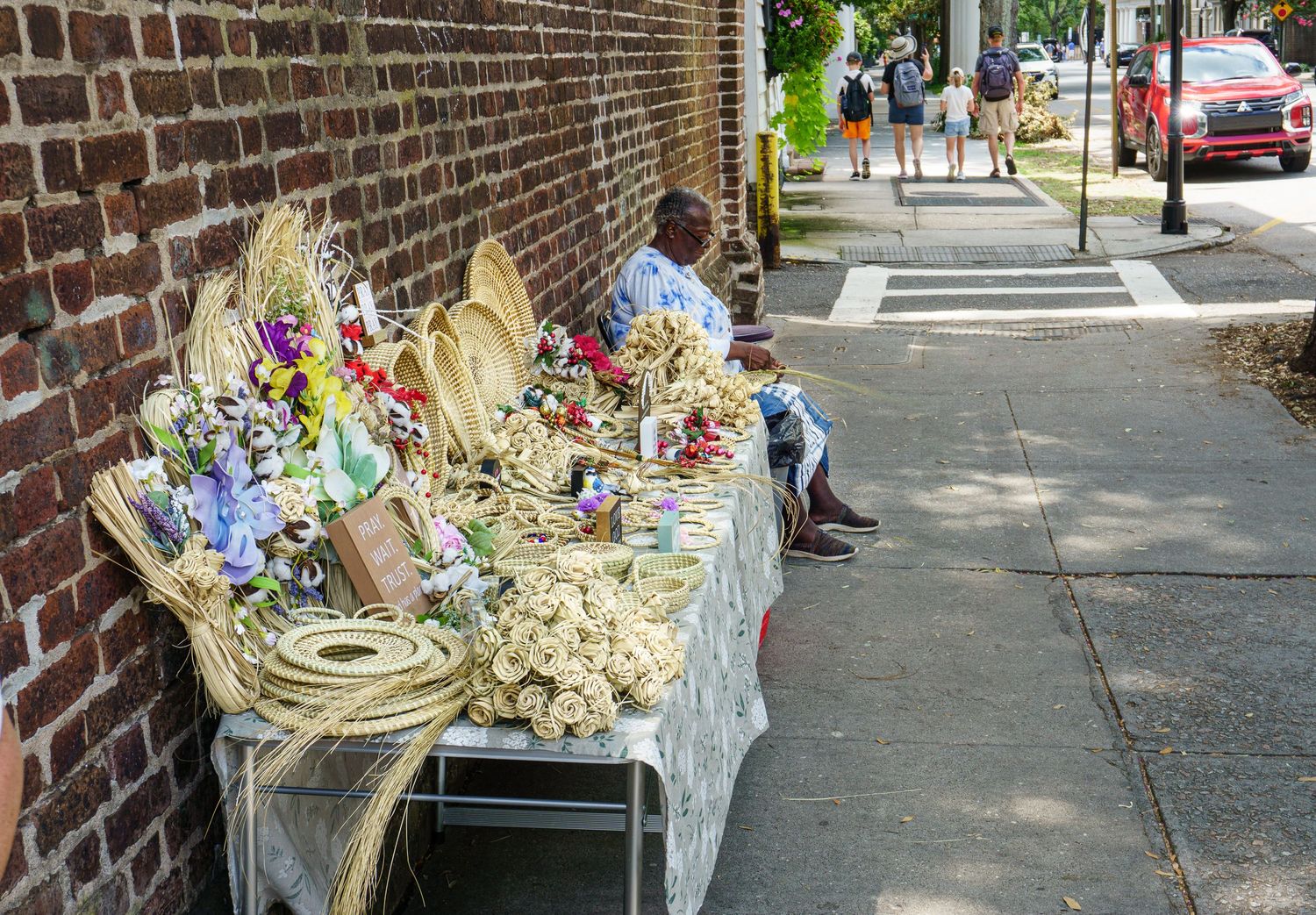 Outdoor sidewalk market with handmade woven baskets and floral crafts displayed on a table against a brick wall.