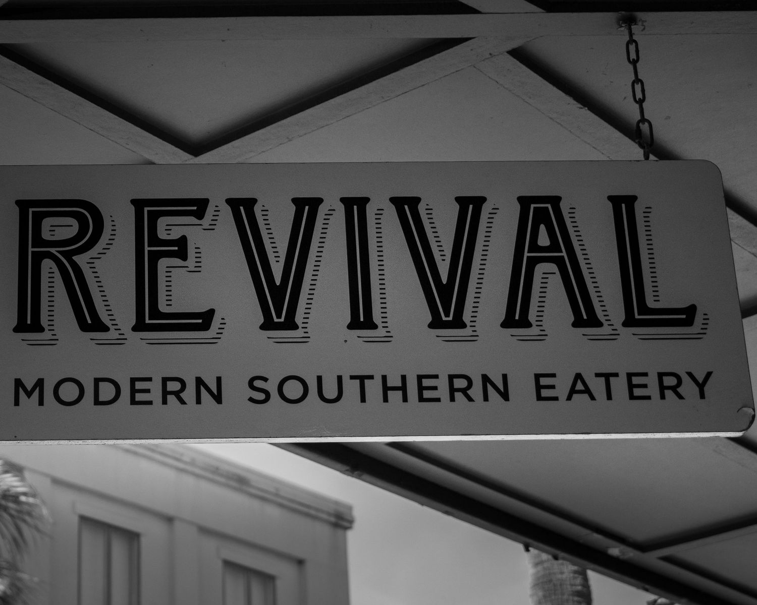 Black and white sign for Revival Modern Southern Eatery restaurant hanging outside a building.