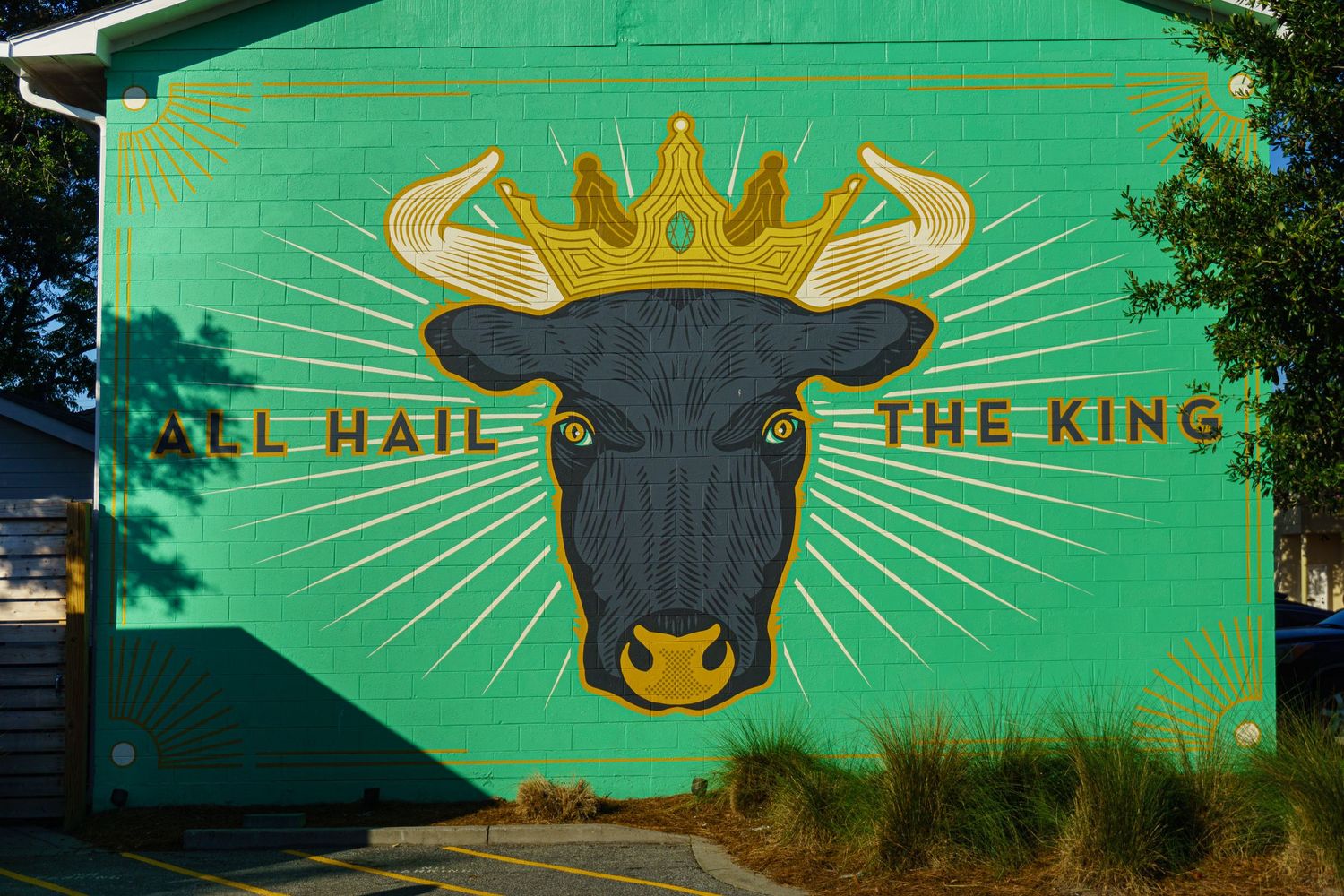 Green mural of a black bull wearing a gold crown with text All Hail The King painted on a building wall.