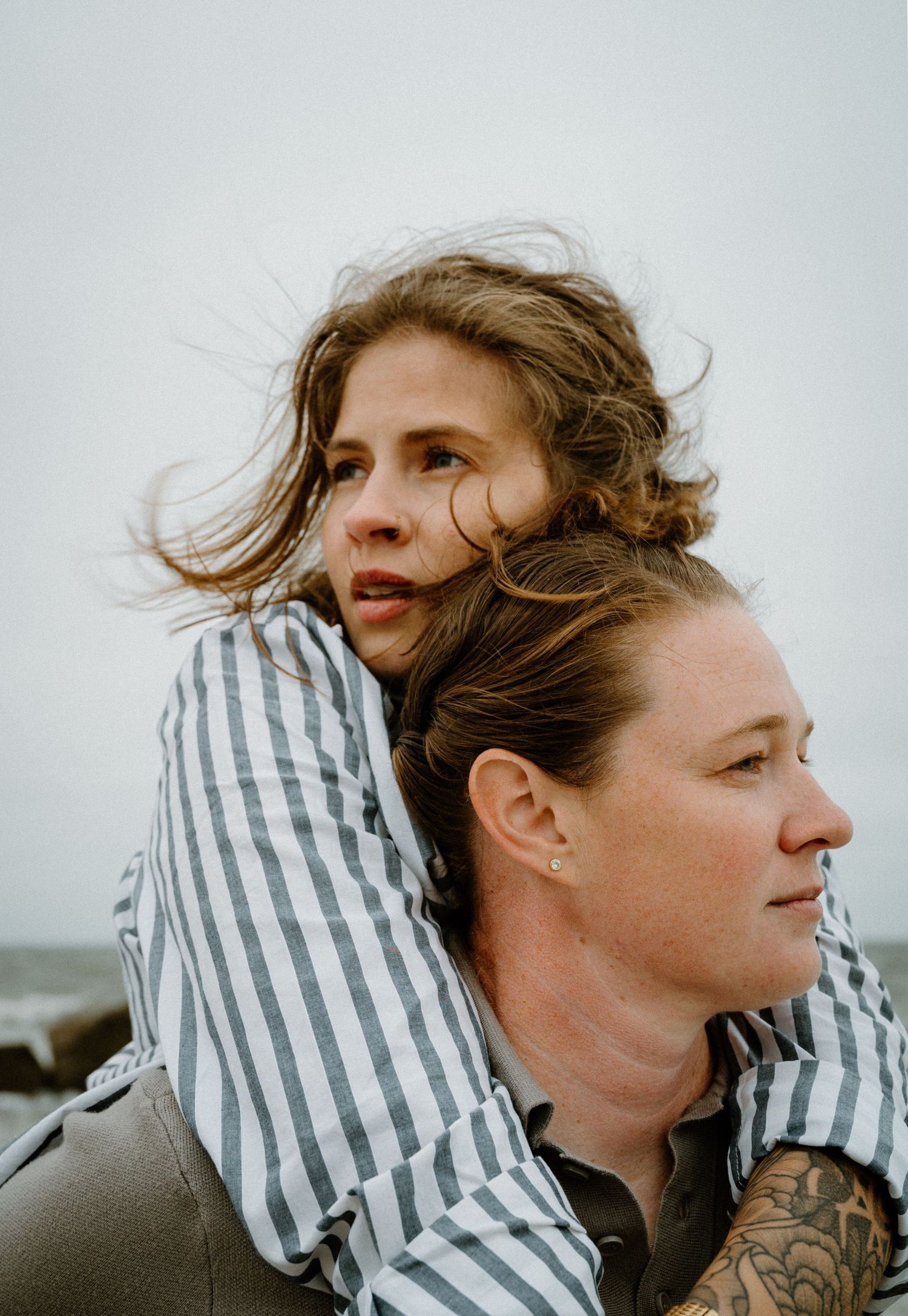 Woman in striped shirt resting on another womans shoulders by the ocean shore on Amelia Island, Florida.