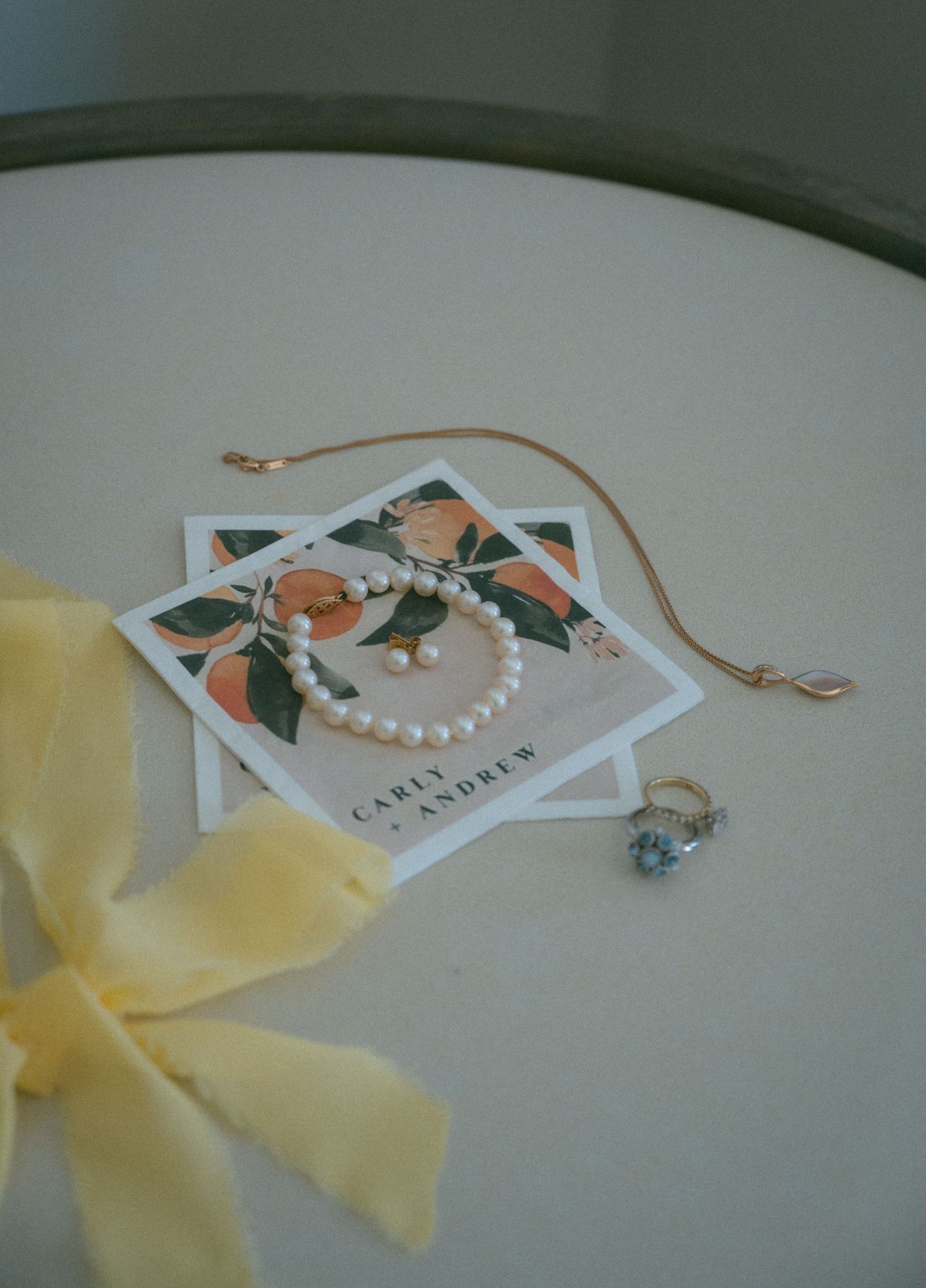 Pearl bracelet and blue gemstone ring beside a gold necklace on a floral wedding invitation card.