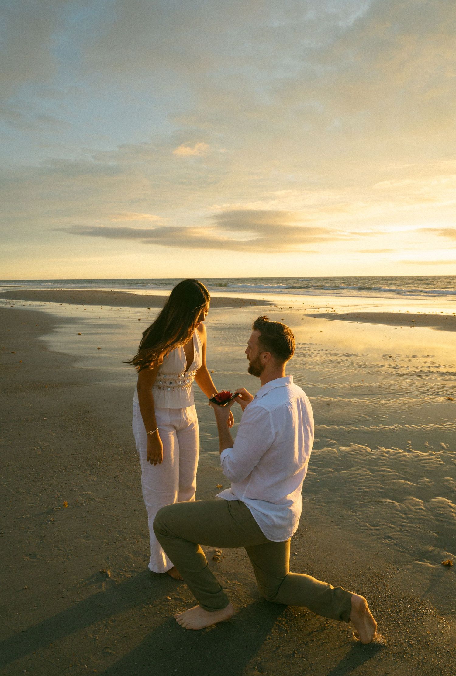 Man proposing on one knee to a woman on a sandy beach at golden sunset in Jacksonville Beach, Florida.