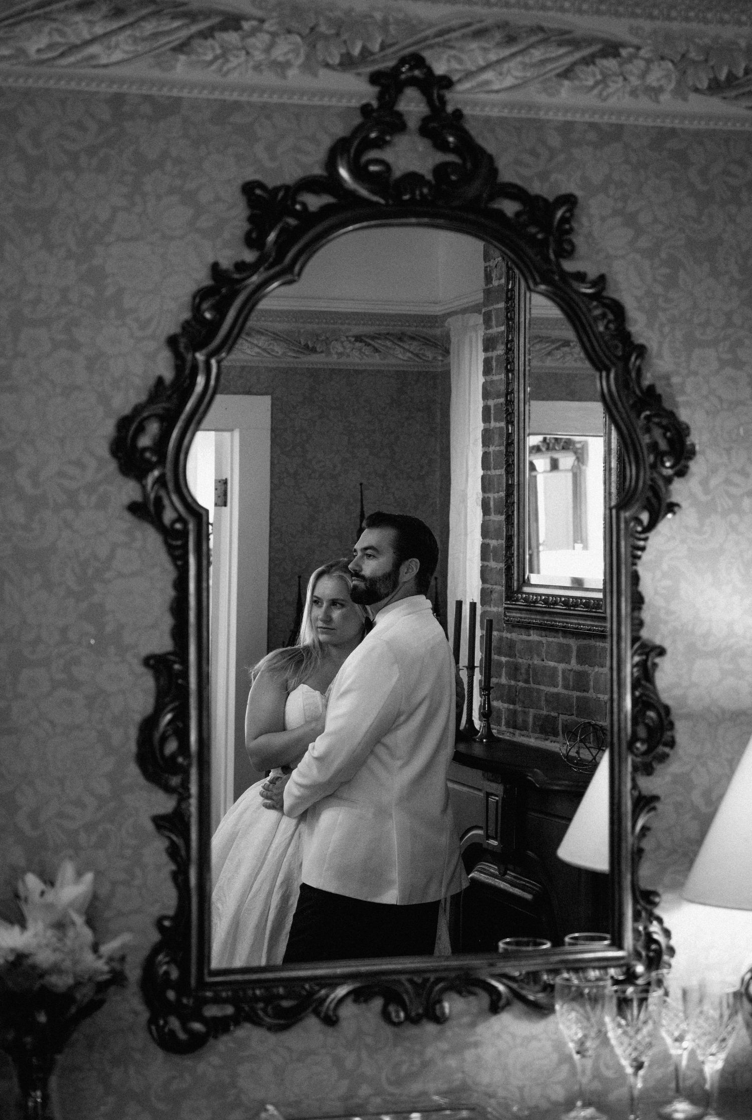 Bride and groom reflected in an ornate vintage mirror in black and white wedding portrait.