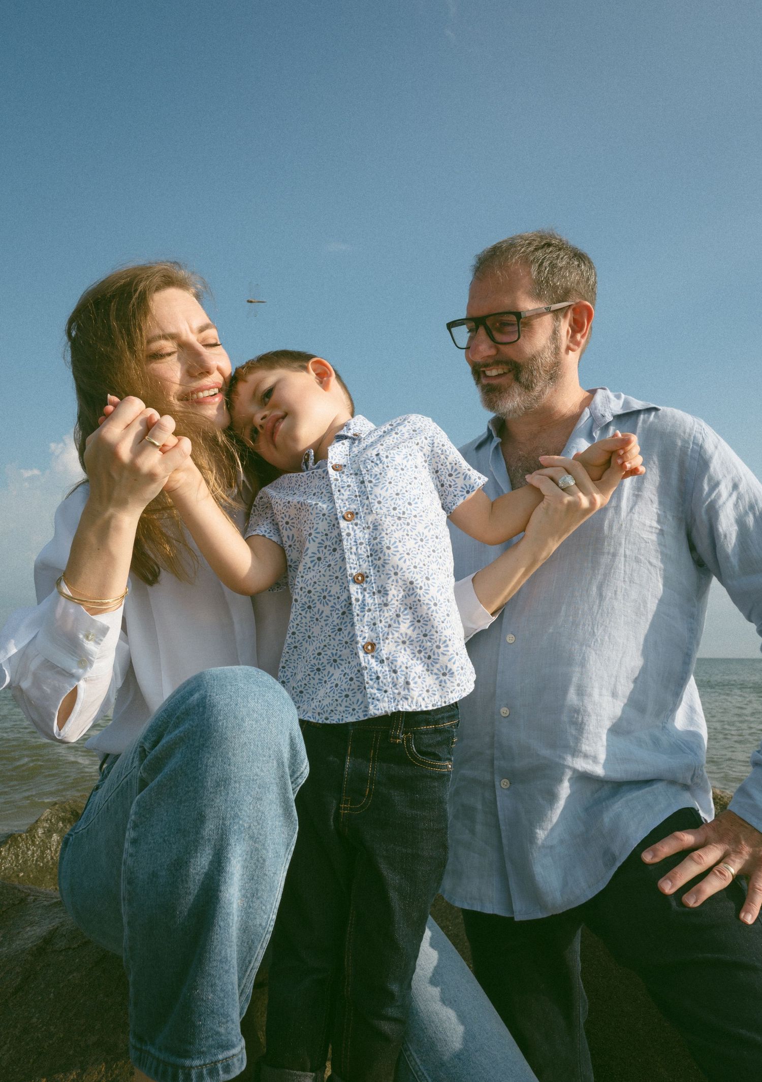 Happy family with young boy laughing together on a sunny beach with blue sky.