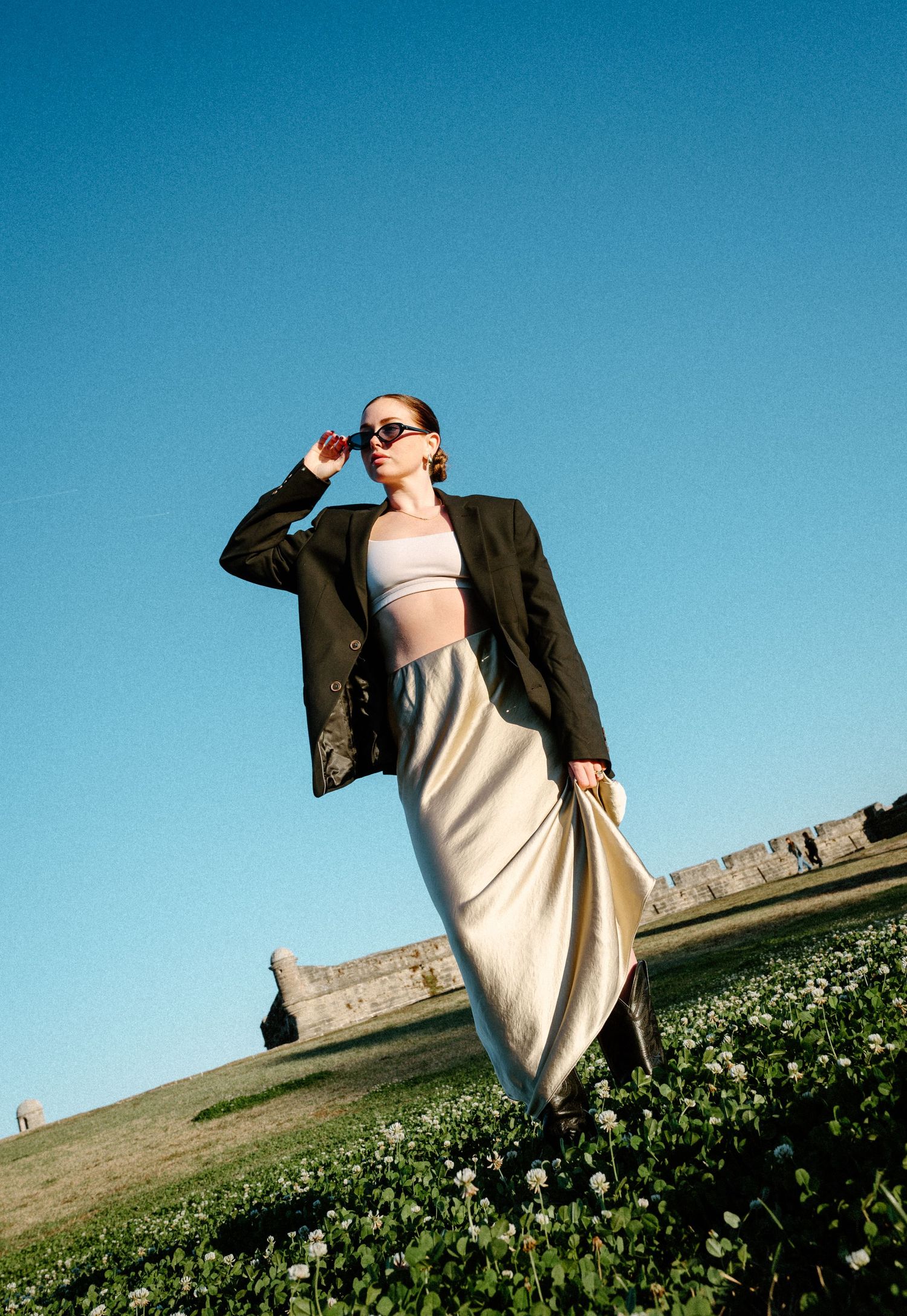 Stylish woman in blazer and satin skirt posing outdoors against a clear blue sky in Saint Augustine, Florida.