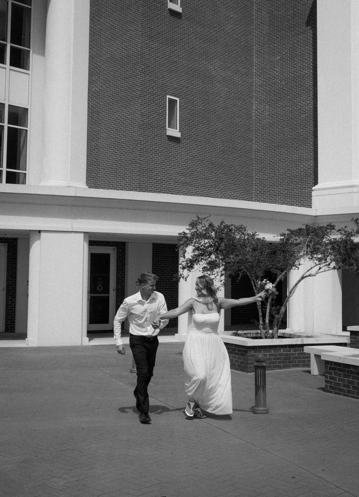 Black and white photo of newlyweds holding hands and running outside courthouse after elopement.